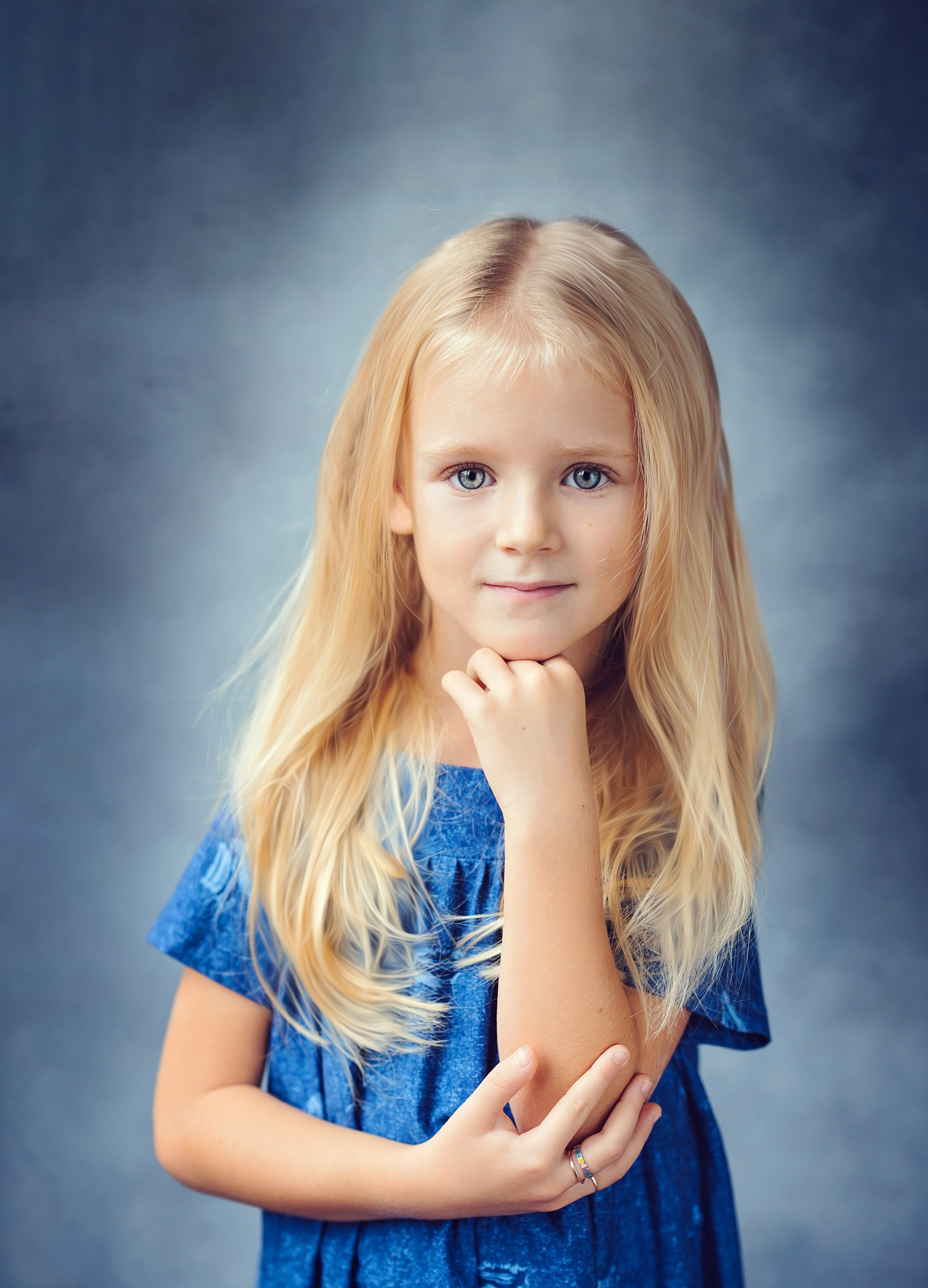 Девочка с длинными светлыми волосами в голубом платье позирует для выпускного альбома подперев руку под подбородком