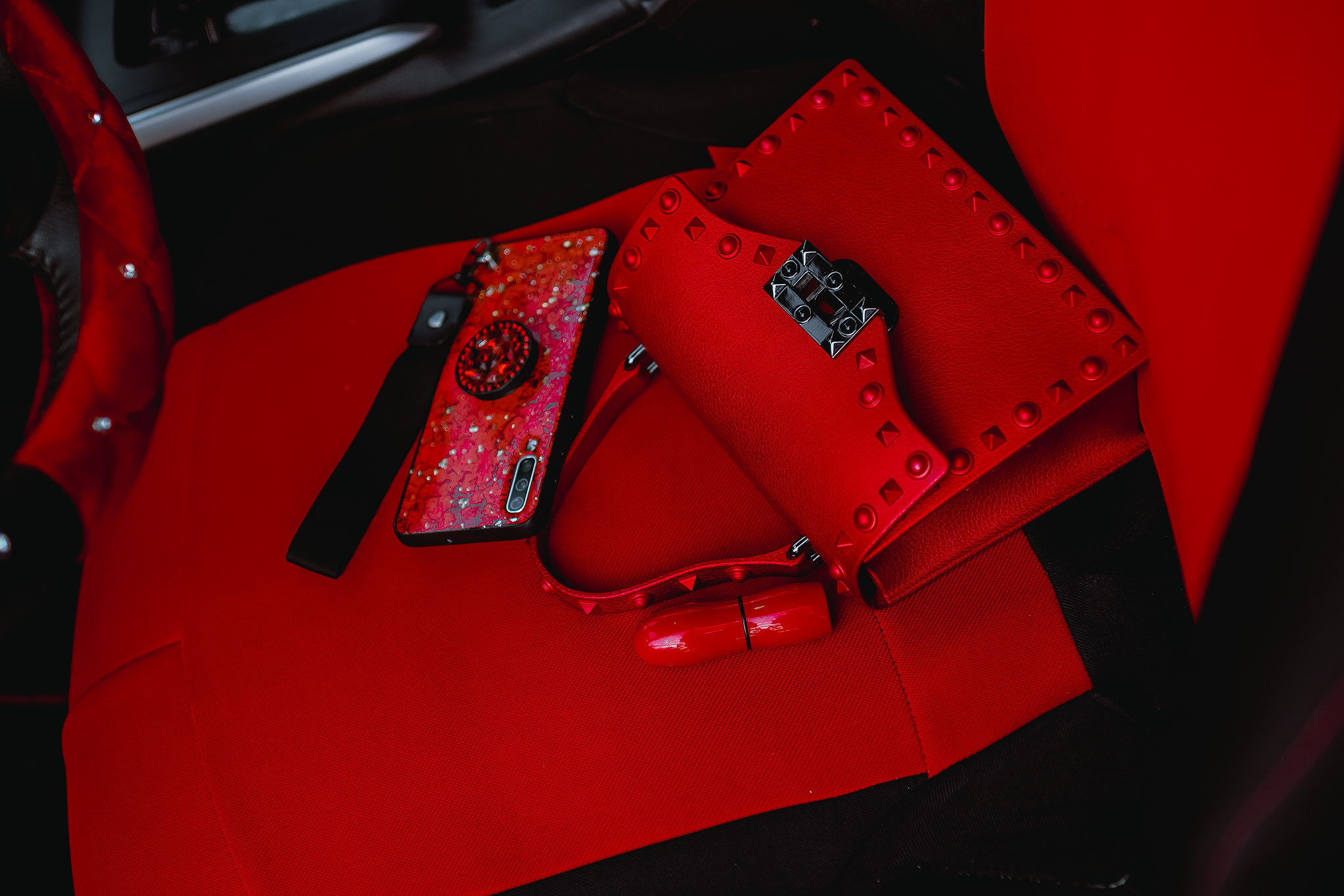 Красный телефон, красная сумочка и красная помада в салоне автомобиля.