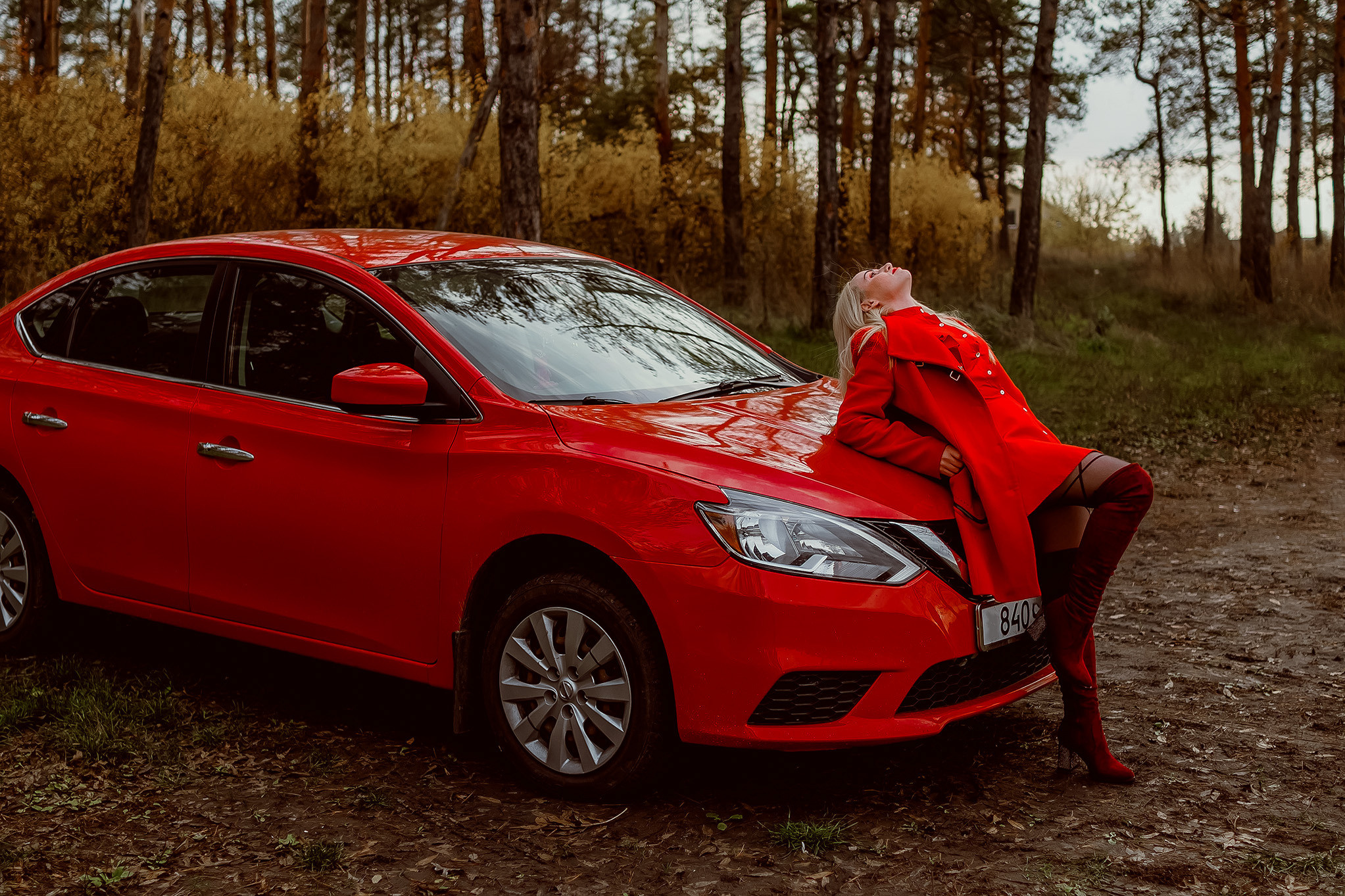 Молодая девушка позирует для фотографа возле красного автомобиля.