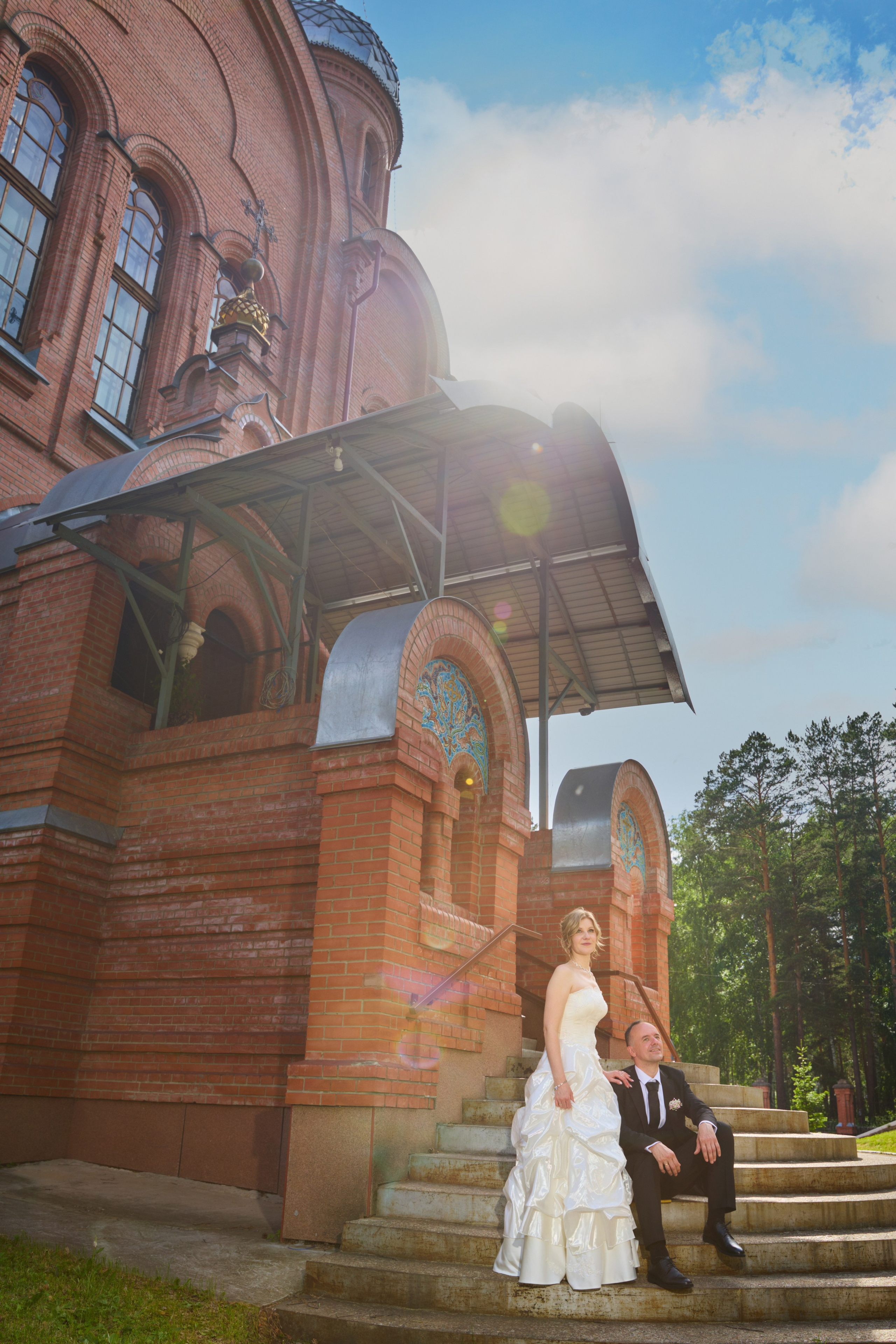 жених сидит на ступеньках церкви обнимая невесту