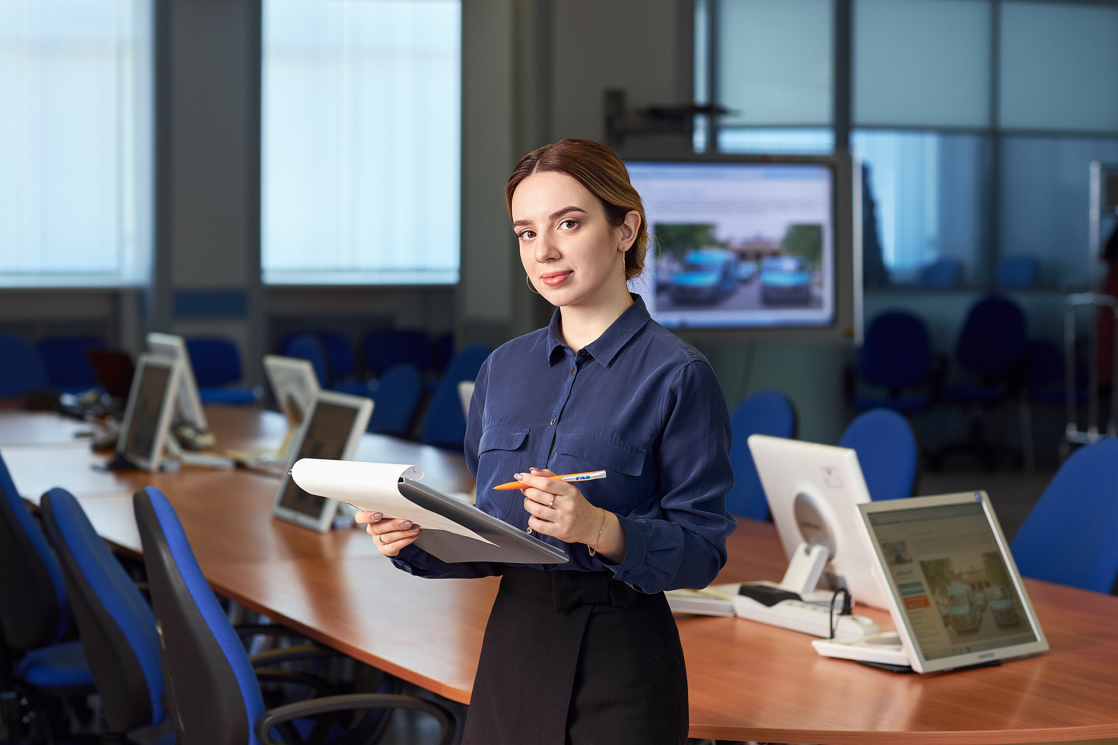 Сотрудница предприятия стоит в конференц зале.