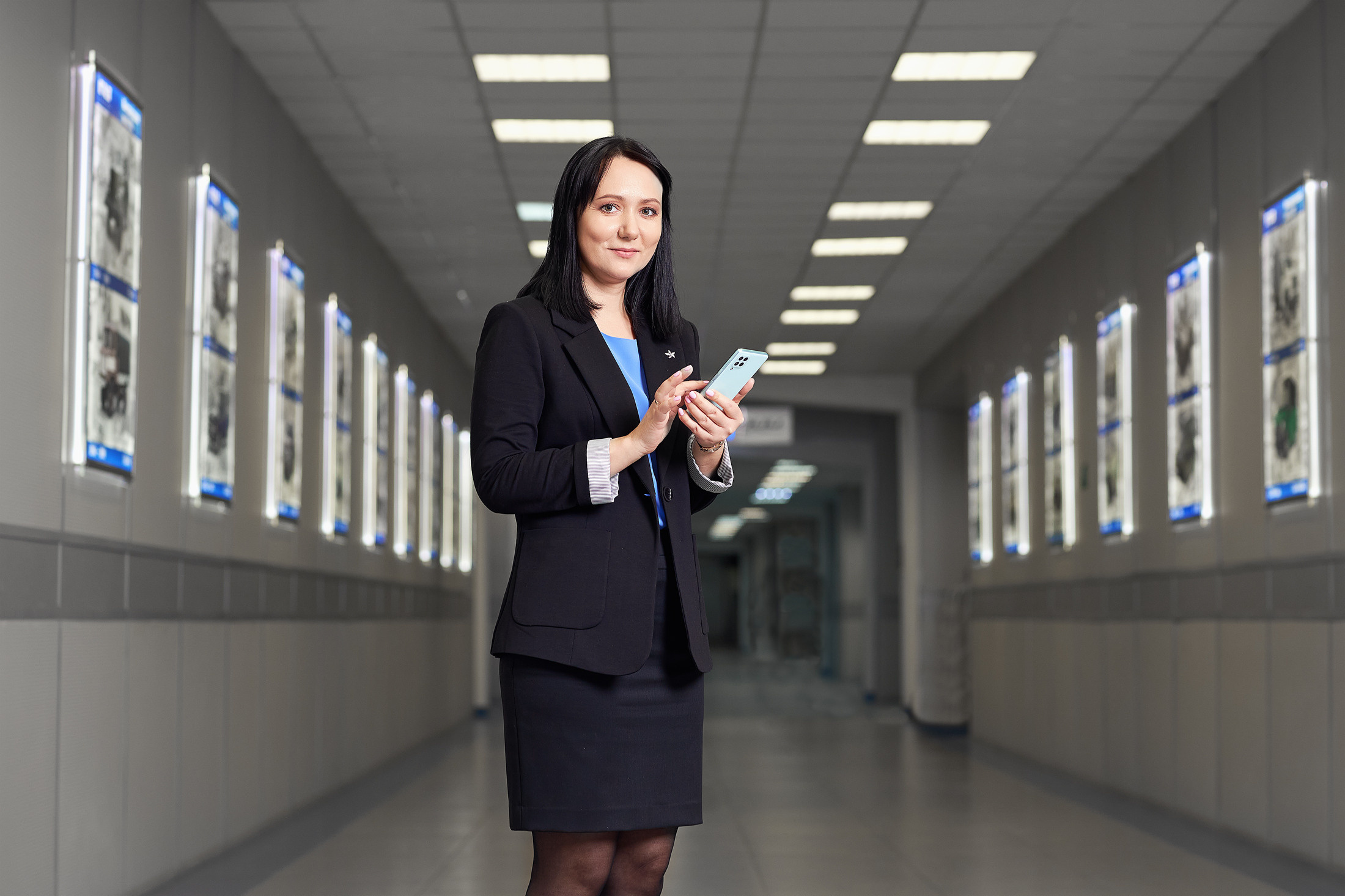 Девушка с блокнотом стоит в коридоре завода.