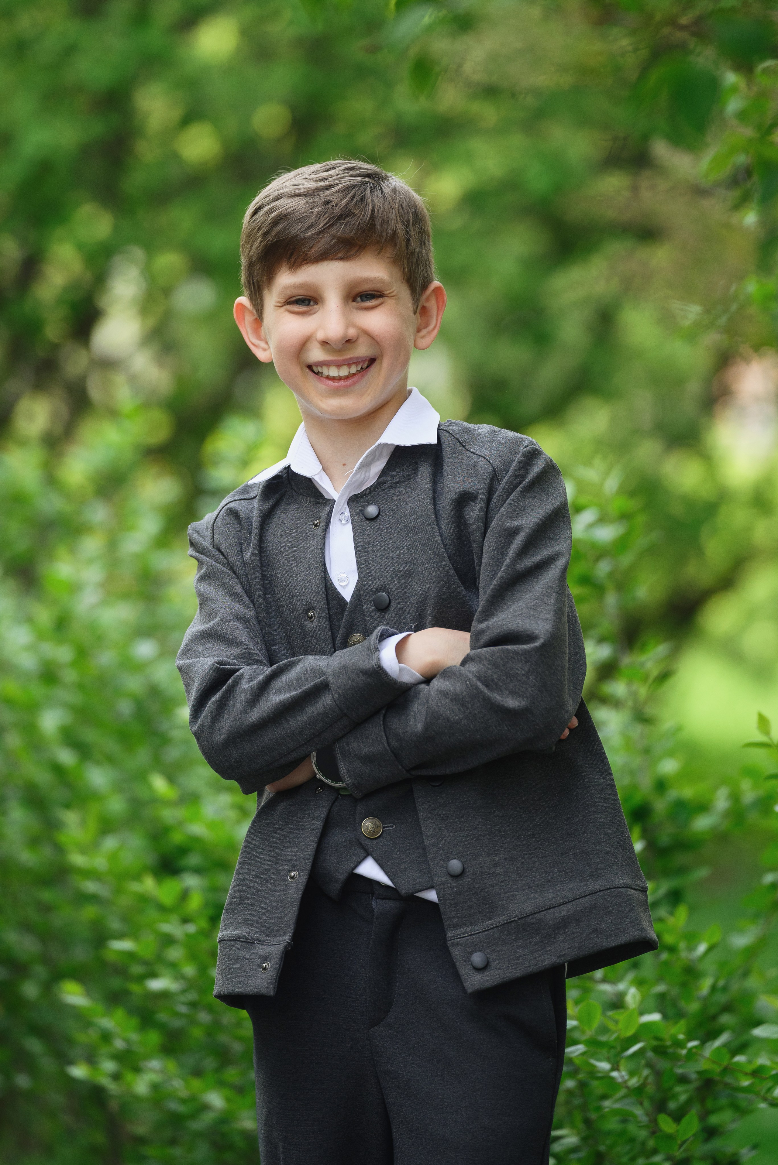 Мальчик в сером костюме на фоне летней зелени
