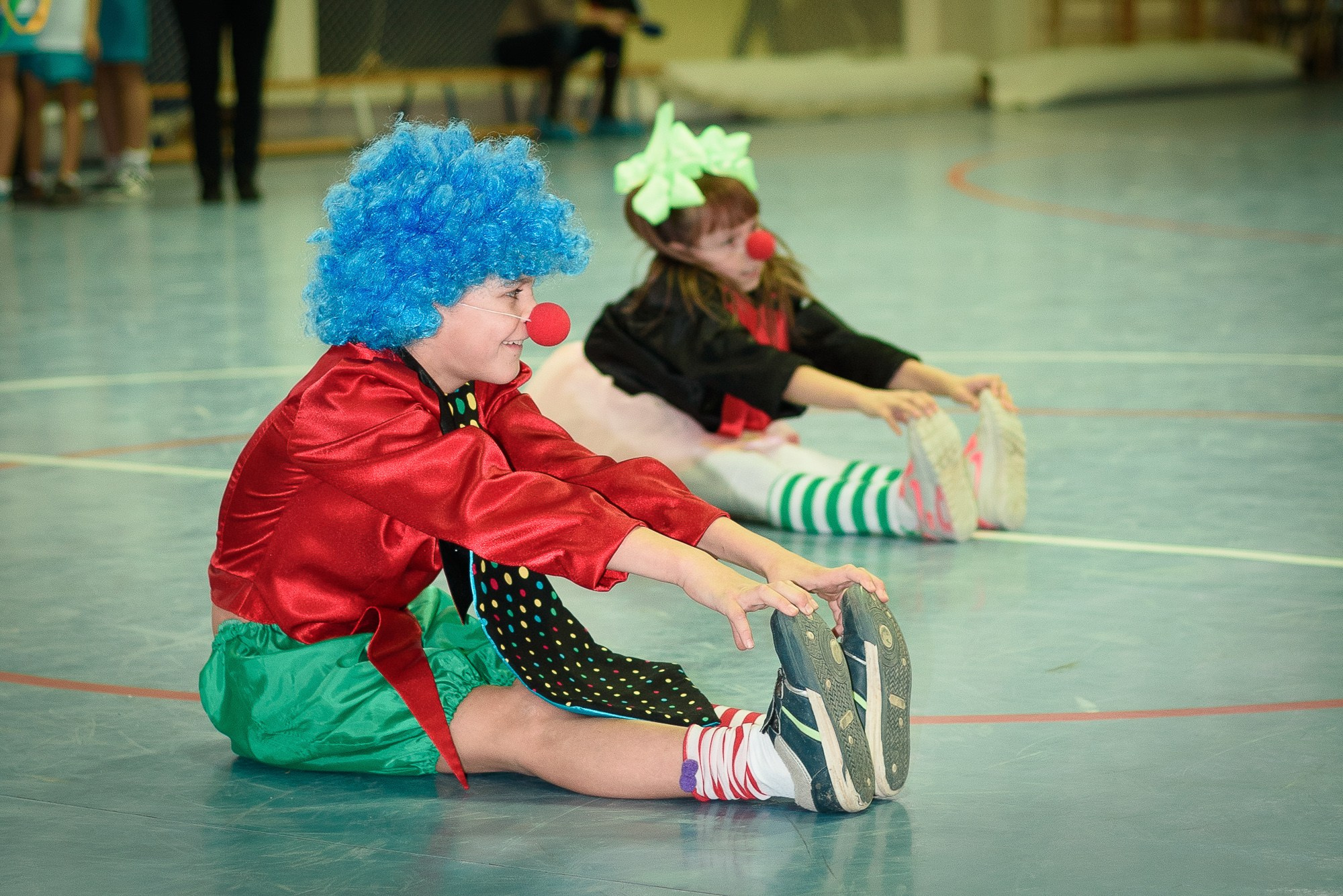 Мальчик в синем парике и с клоунским  носом сидит на полу спортзала