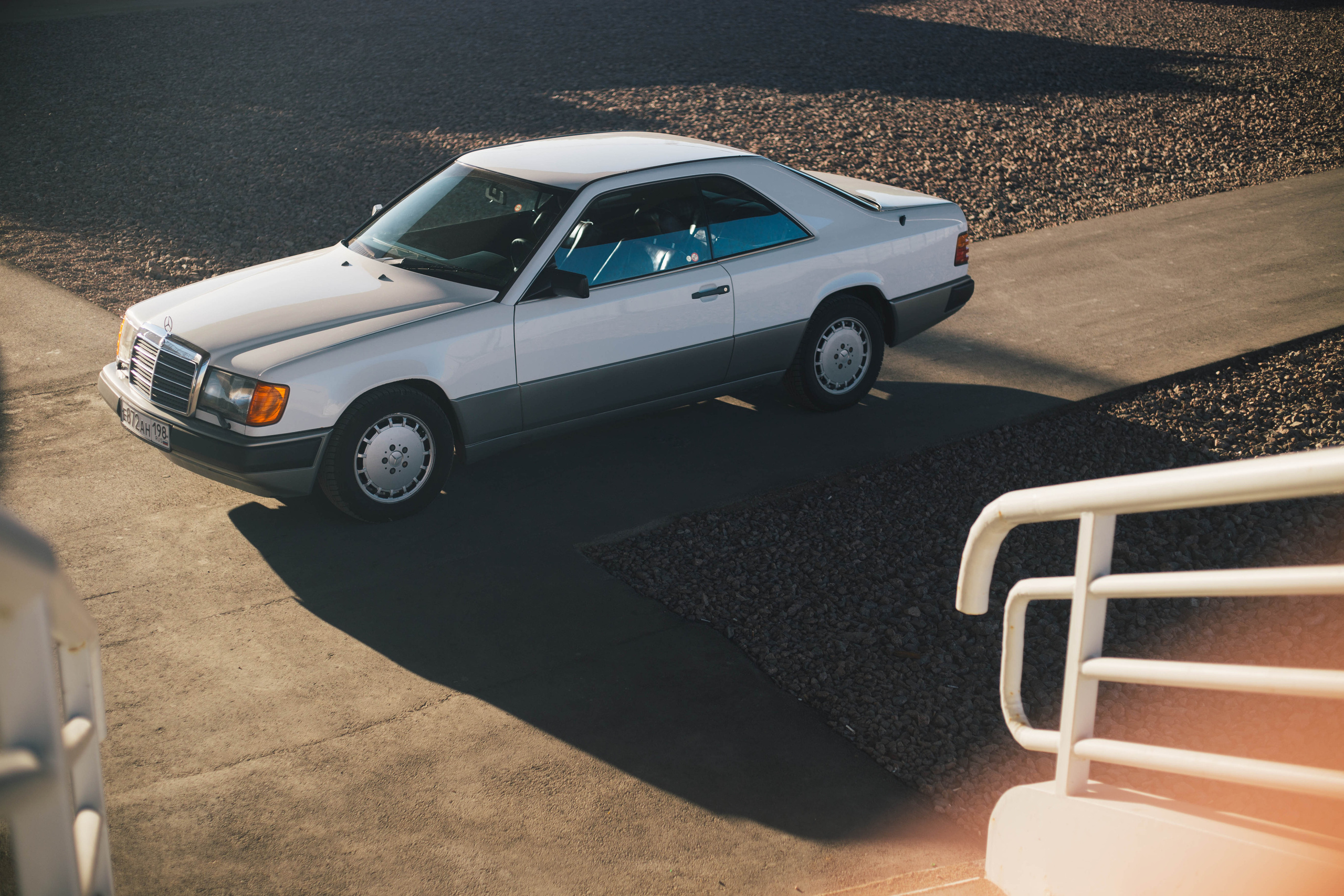 Белый мерседес 124 в редком кузове купе на фоне моста в Санкт-Петербурге