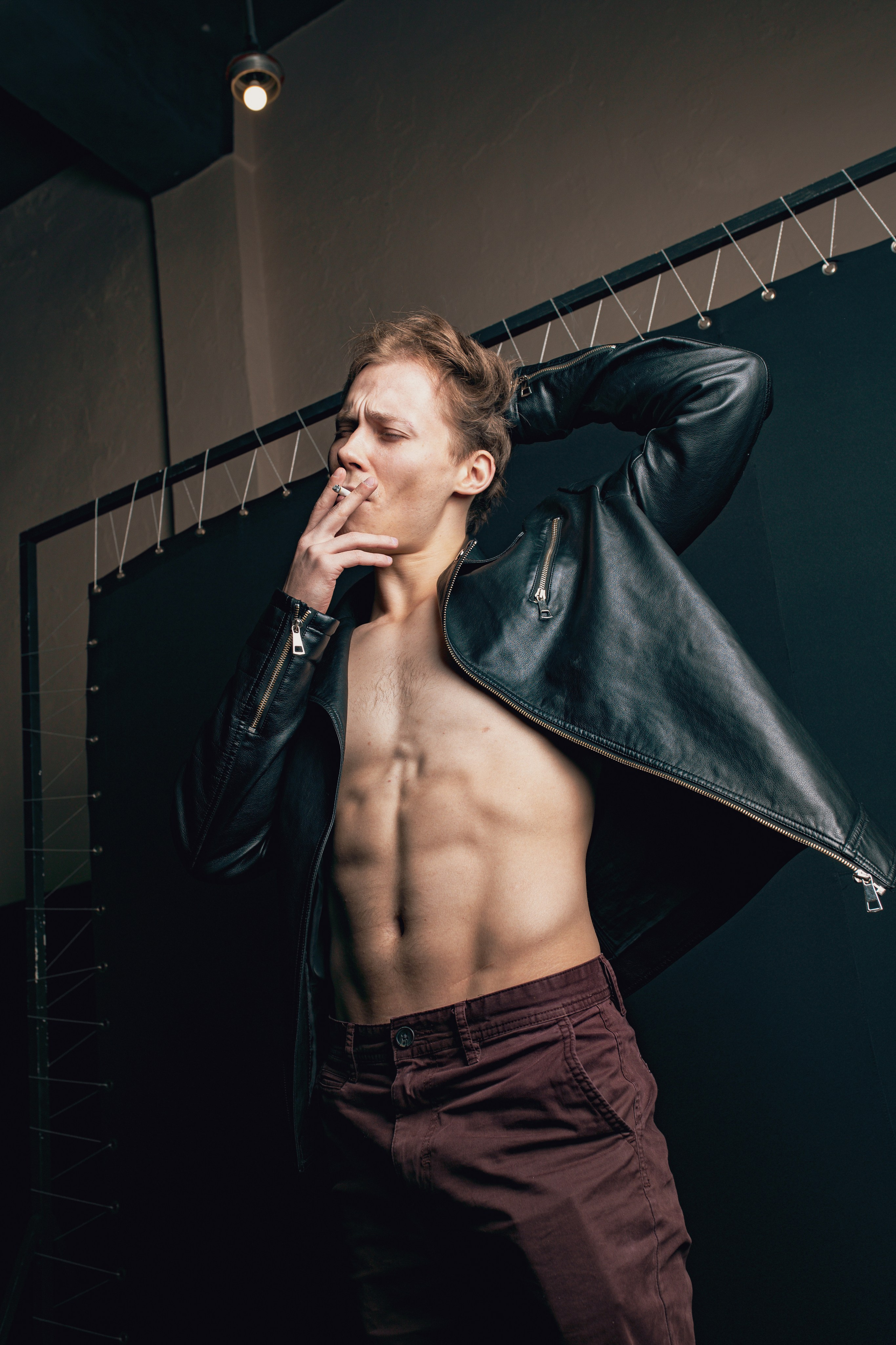 Брутальный парень курит сигарету в кожаной куртке и с голым торсом