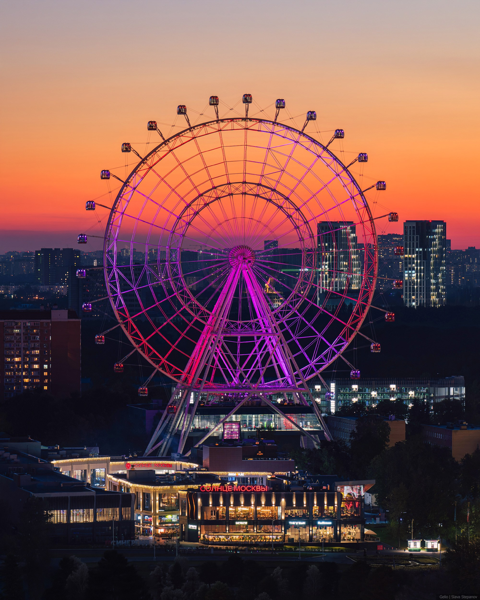 "Sun of Moscow" Ferris wheel with bright purple illumination against the night city blocks, by Slava Stepanov.