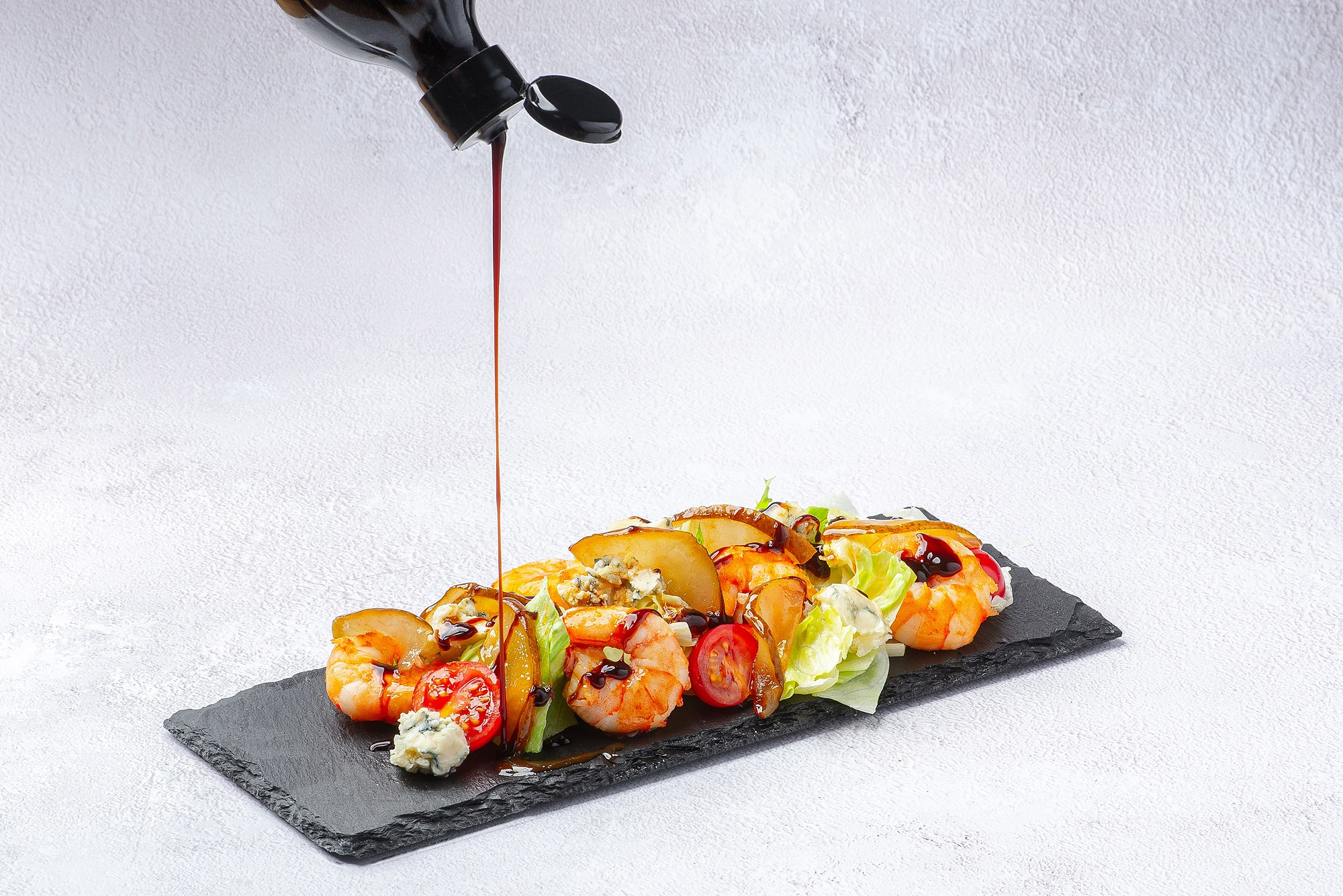 Салат из креветок поливают соусом на белом фоне