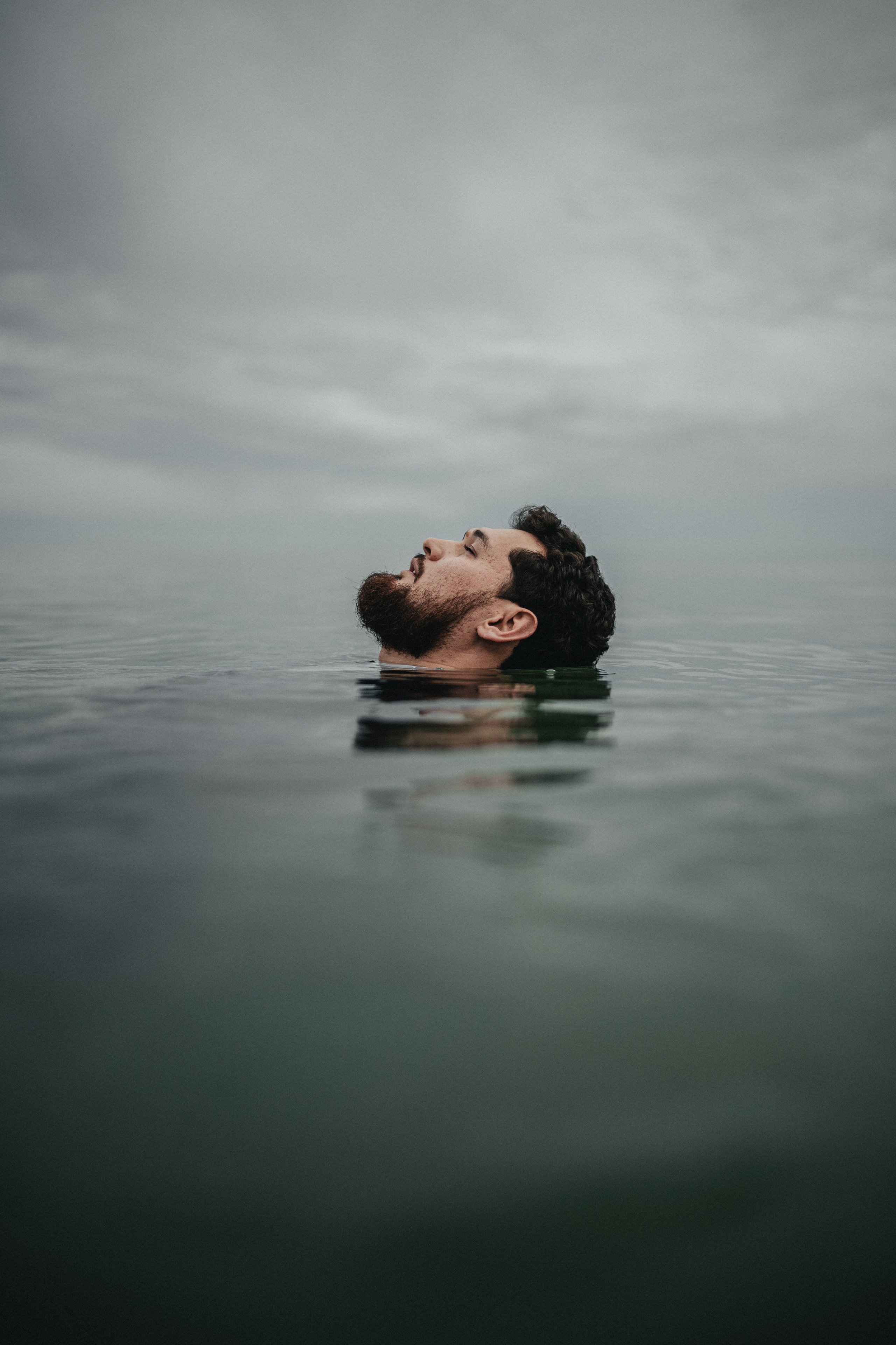 Мужчина в костюме плавает в воде, его голова едва видна над поверхностью