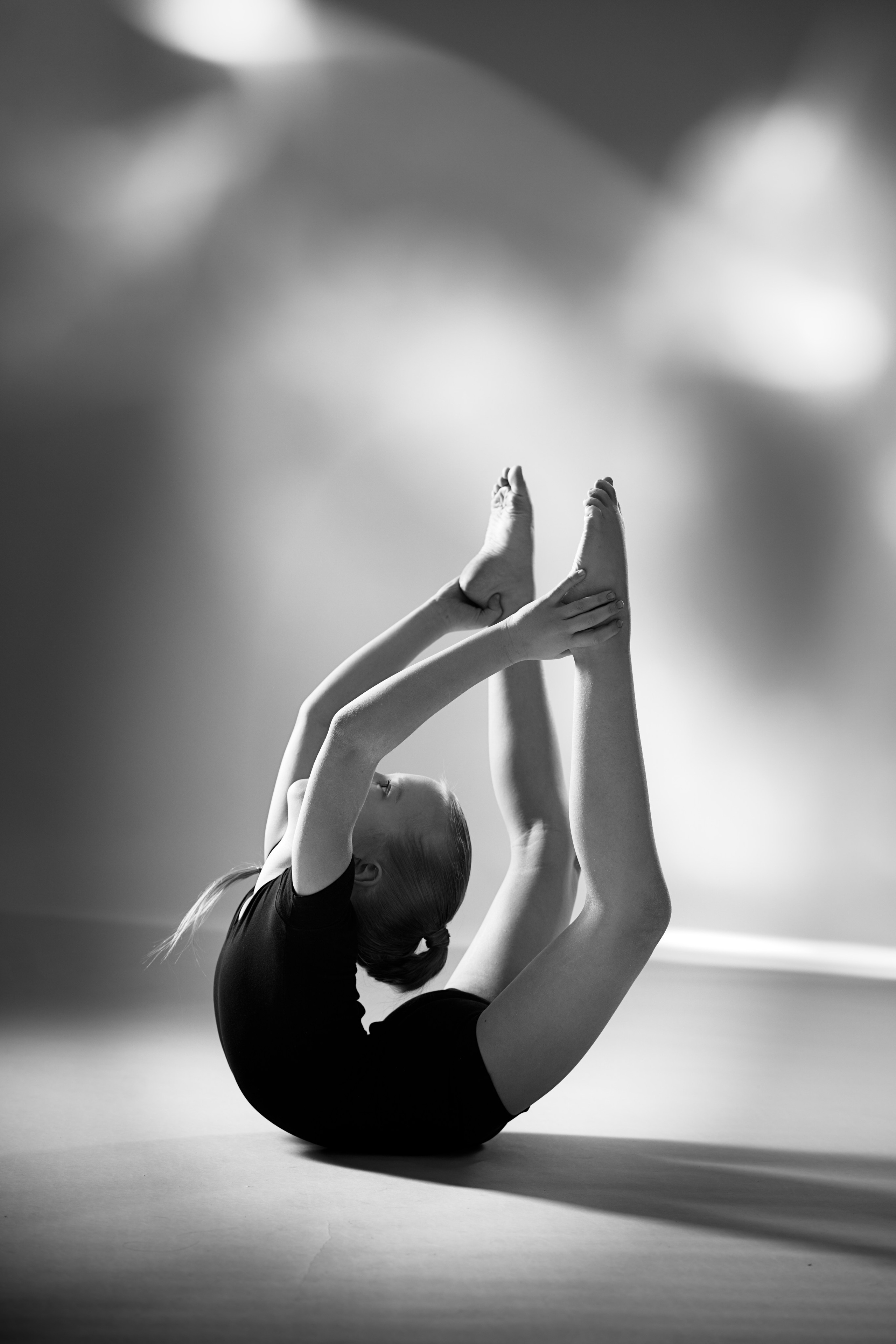 Черно-белое фото юной гимнастки в глубокой складке на полу, художественная гимнастика в стиле спортарт, акцент на гибкости