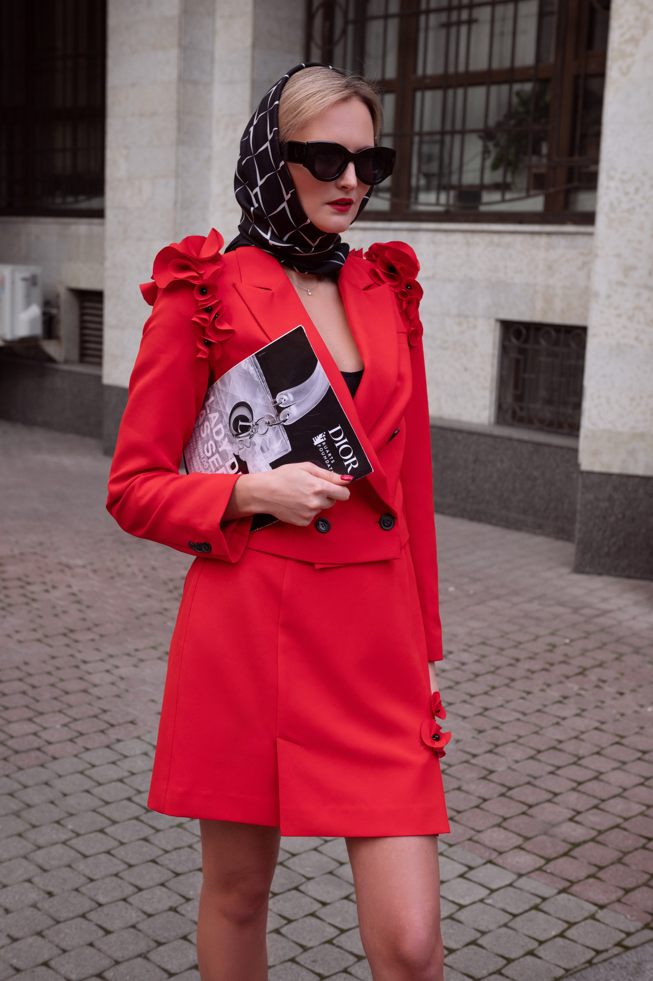 Уличное фото для контента: девушка в черном платке и черных очках, на ней эффектный красный костюм. Фото в стиле фэшн. Съемка для бренда
