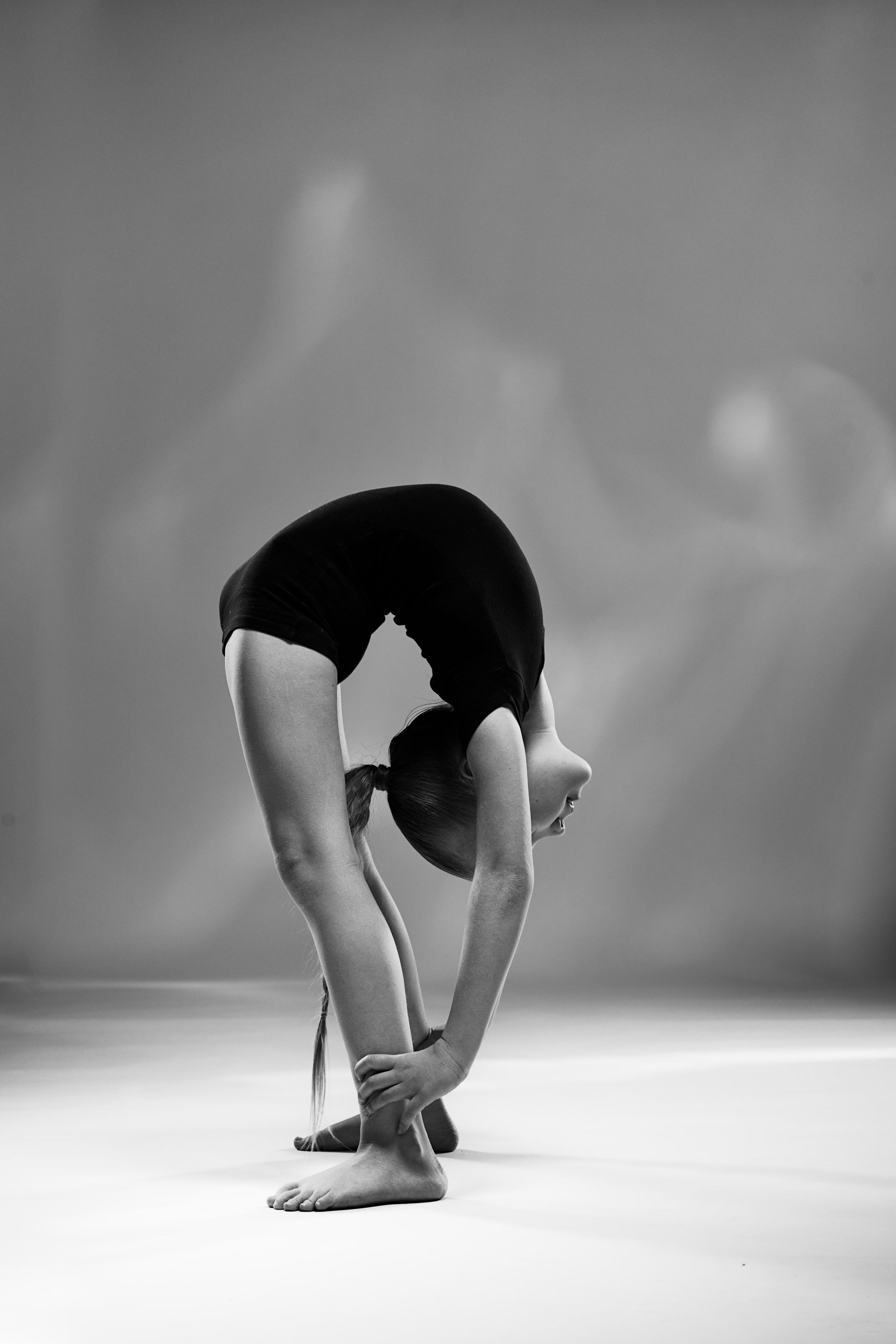 Черно-белый художественный портрет гимнастки, выполняющей глубокий наклон.