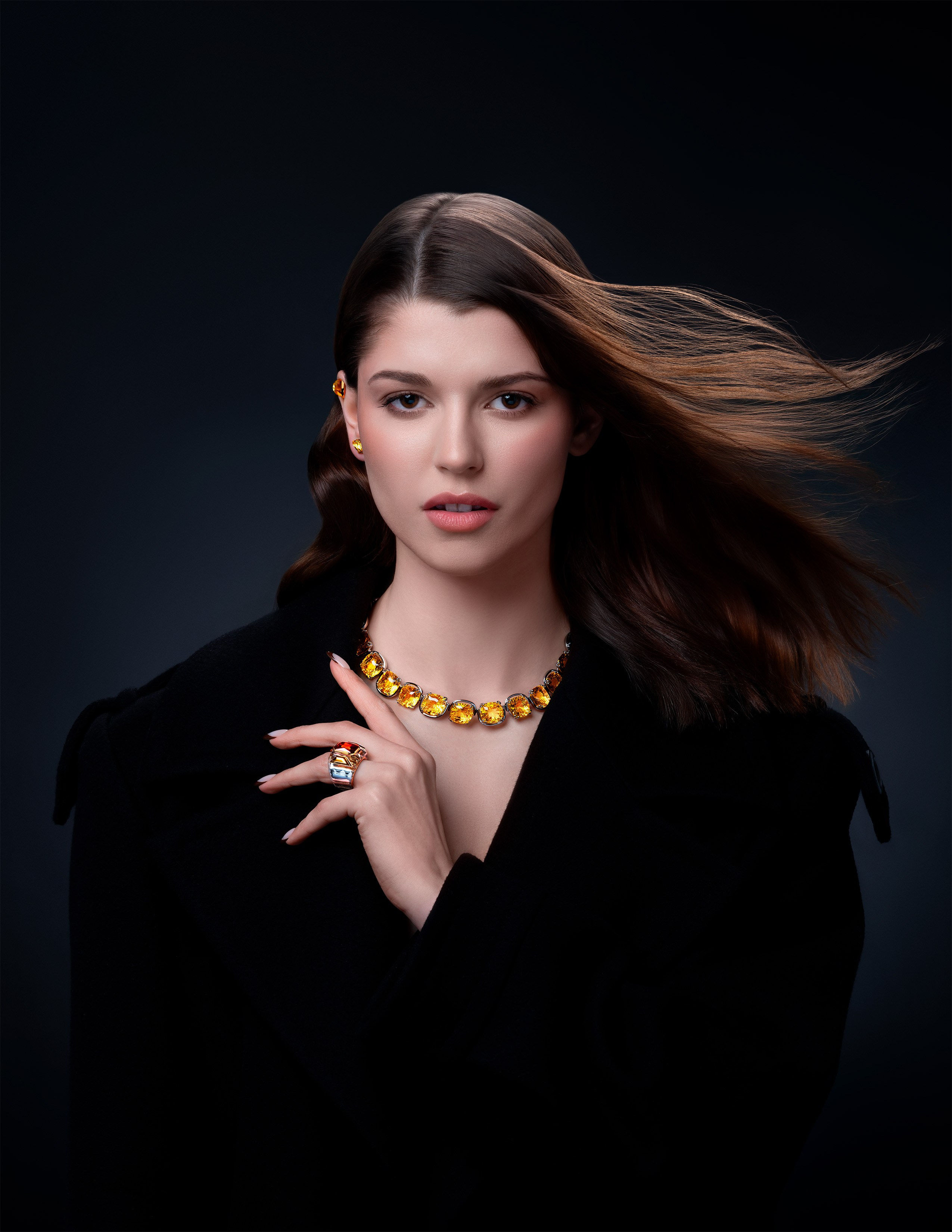 Dynamic fashion portrait of a model wearing Swarovski jewelry – bold yellow gemstone necklace and gold ring styled for high-end glamour.