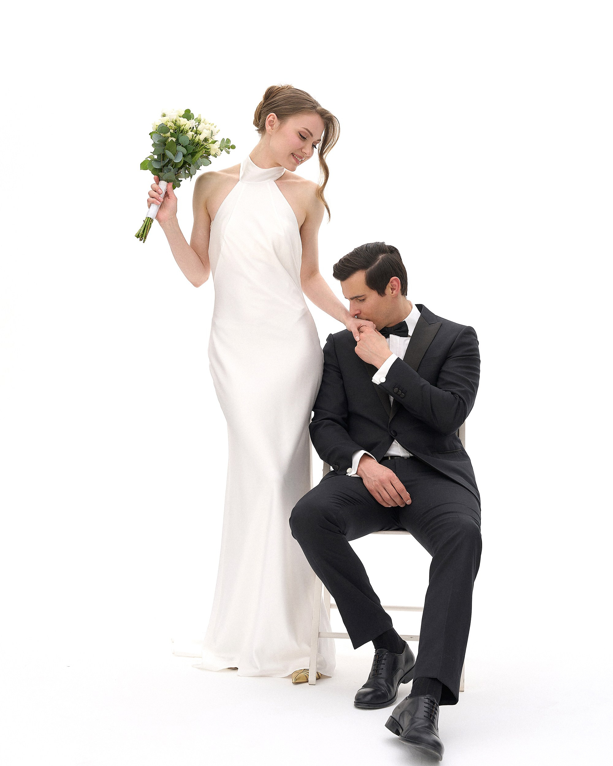 Душевный момент: невеста стоит, жених сидит и целует ей руку. Белый фон студии, ничто не отвлекает от чувств. Минималистичная свадебная съемка, фотограф Дмитрий Цветков, Санкт-Петербург