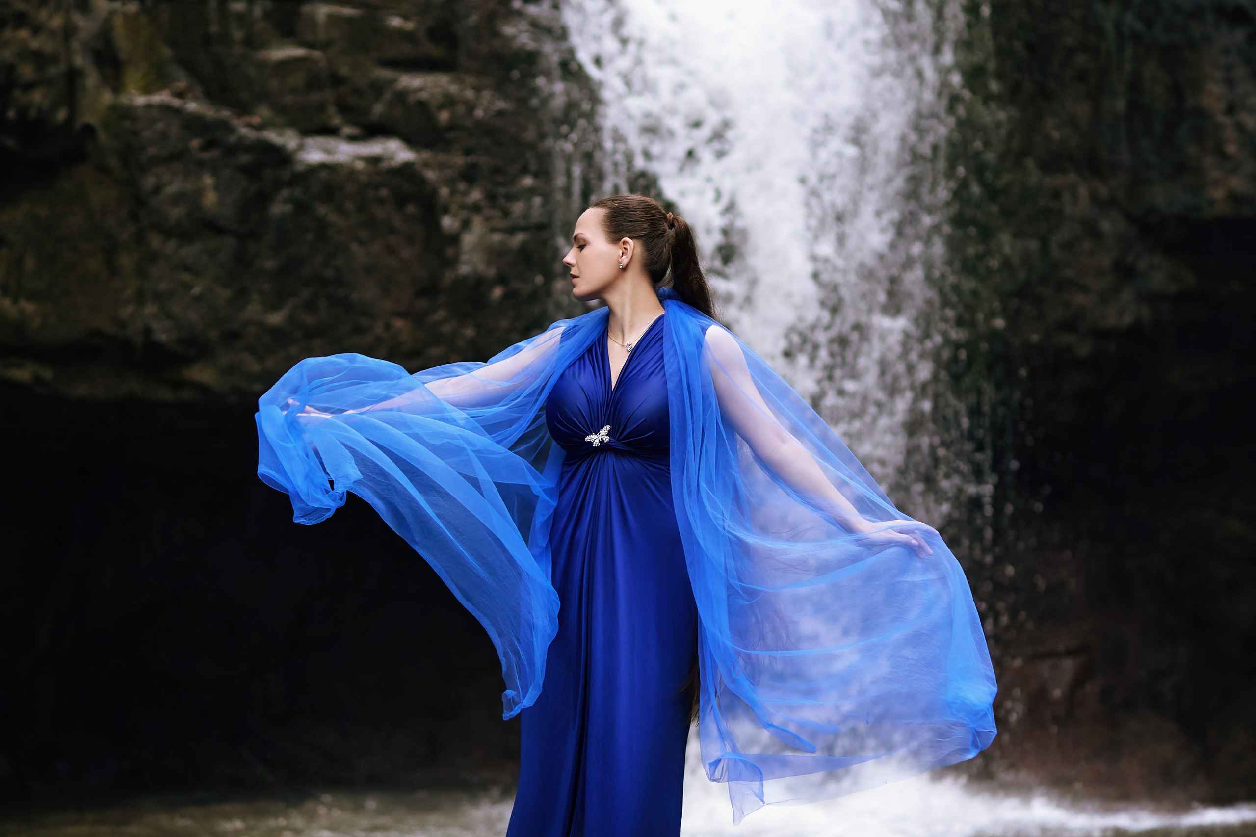 Портретная фотосессия для женщины в синем платье, позирующей на фоне водопада