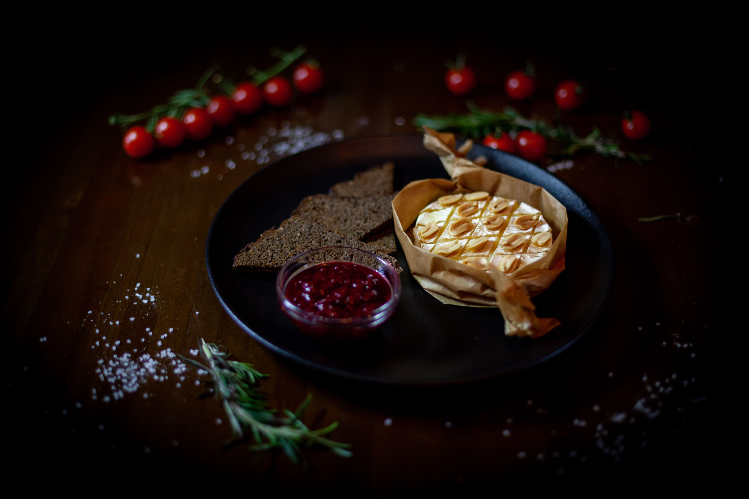 Сыр камамбер, сопровождаемый малиновым соусом, украшает деревянную доску, окруженный свежими фруктами и орехами