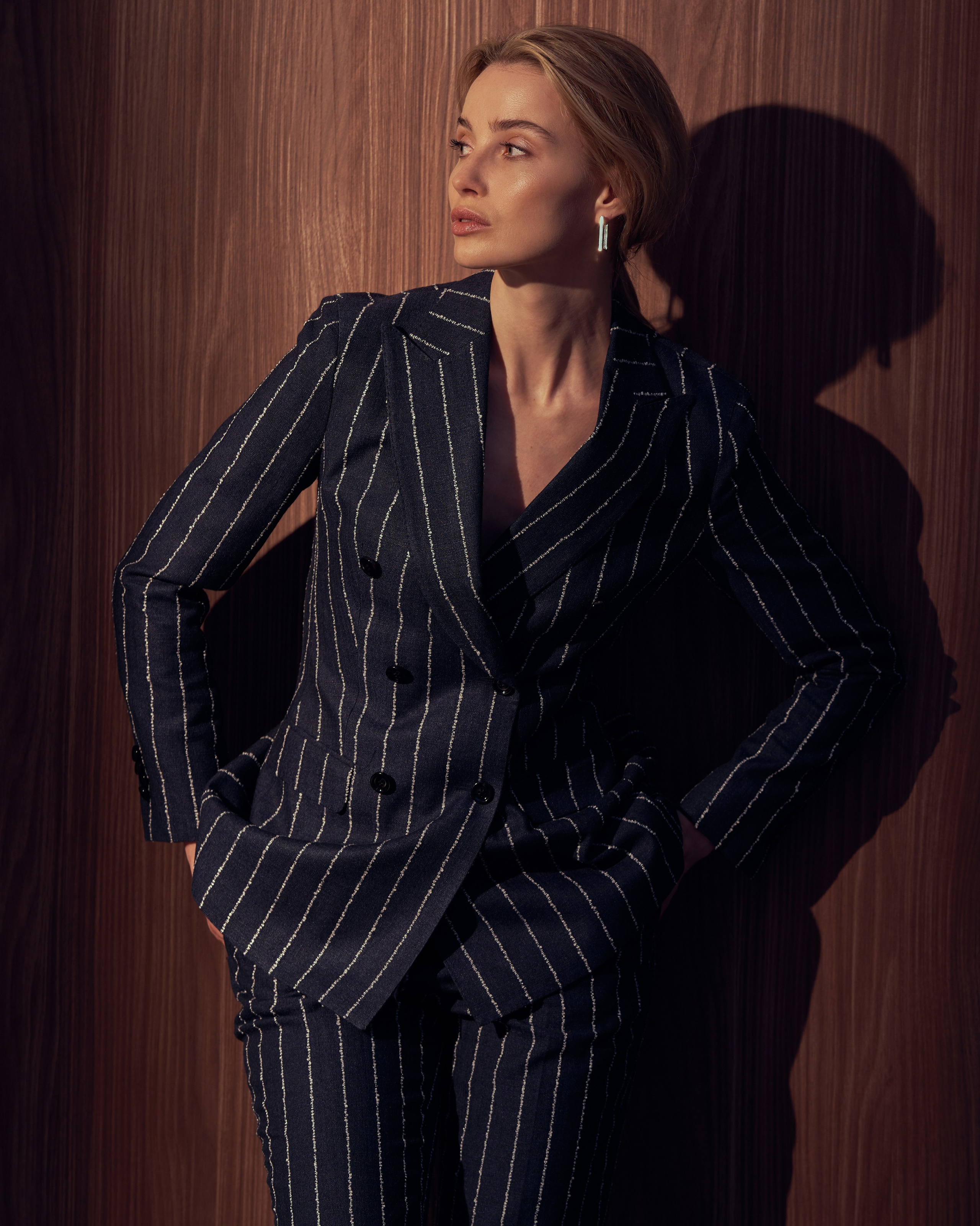 Съемка одежды, девушка на фоне деревянной стены в брючном костюме в полоску и кедах, девушка в костюме и кедах.