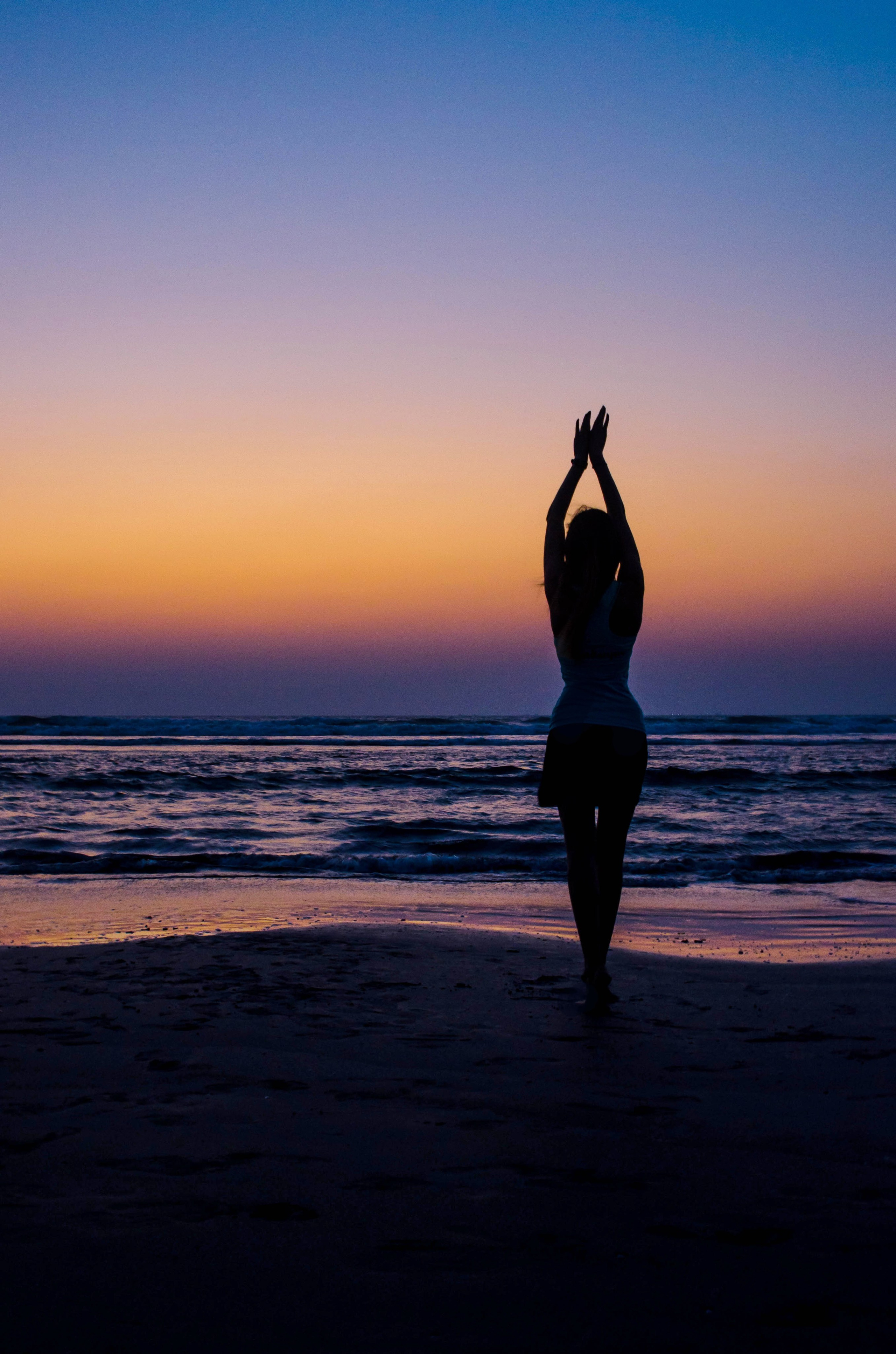 силуэт стройной девушки на фоне красивого морского заката в голубой синий час фотографии