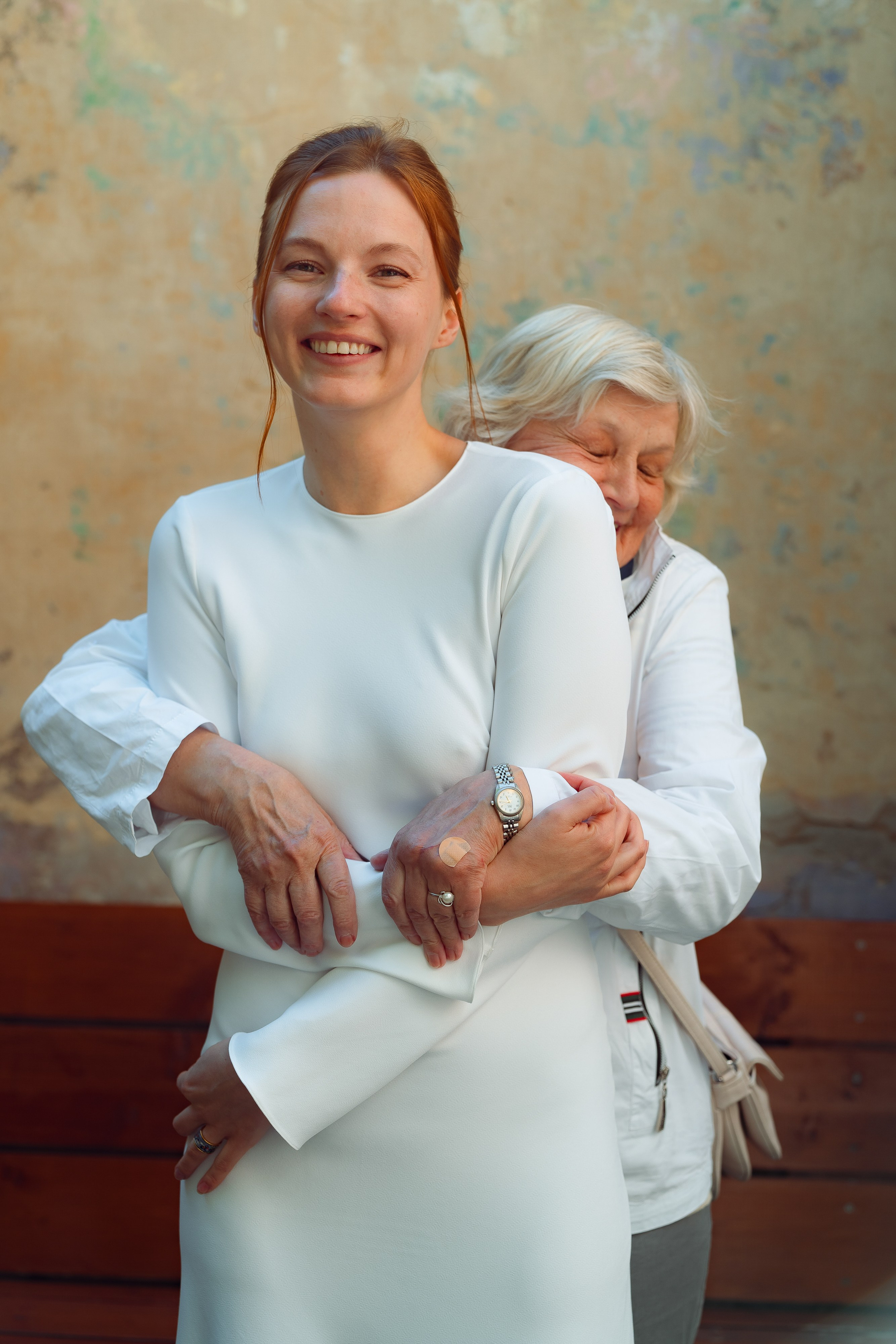 Невеста смеётся, бабушка обнимает её у стены с бирюзовой патиной