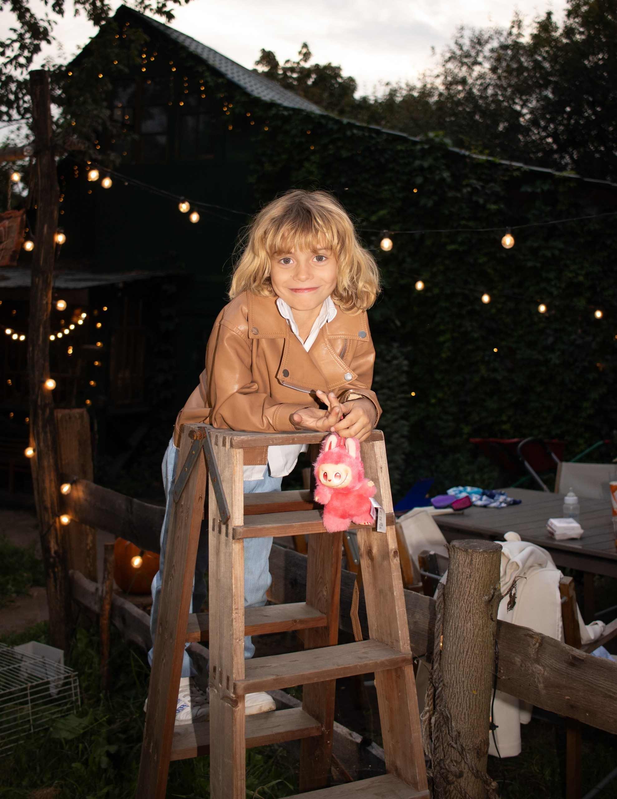 Ребёнок в кожаной куртке сидит на деревянной лестнице на фоне гирлянд — детская осенняя фотосессия, фотограф Карасёва Елена