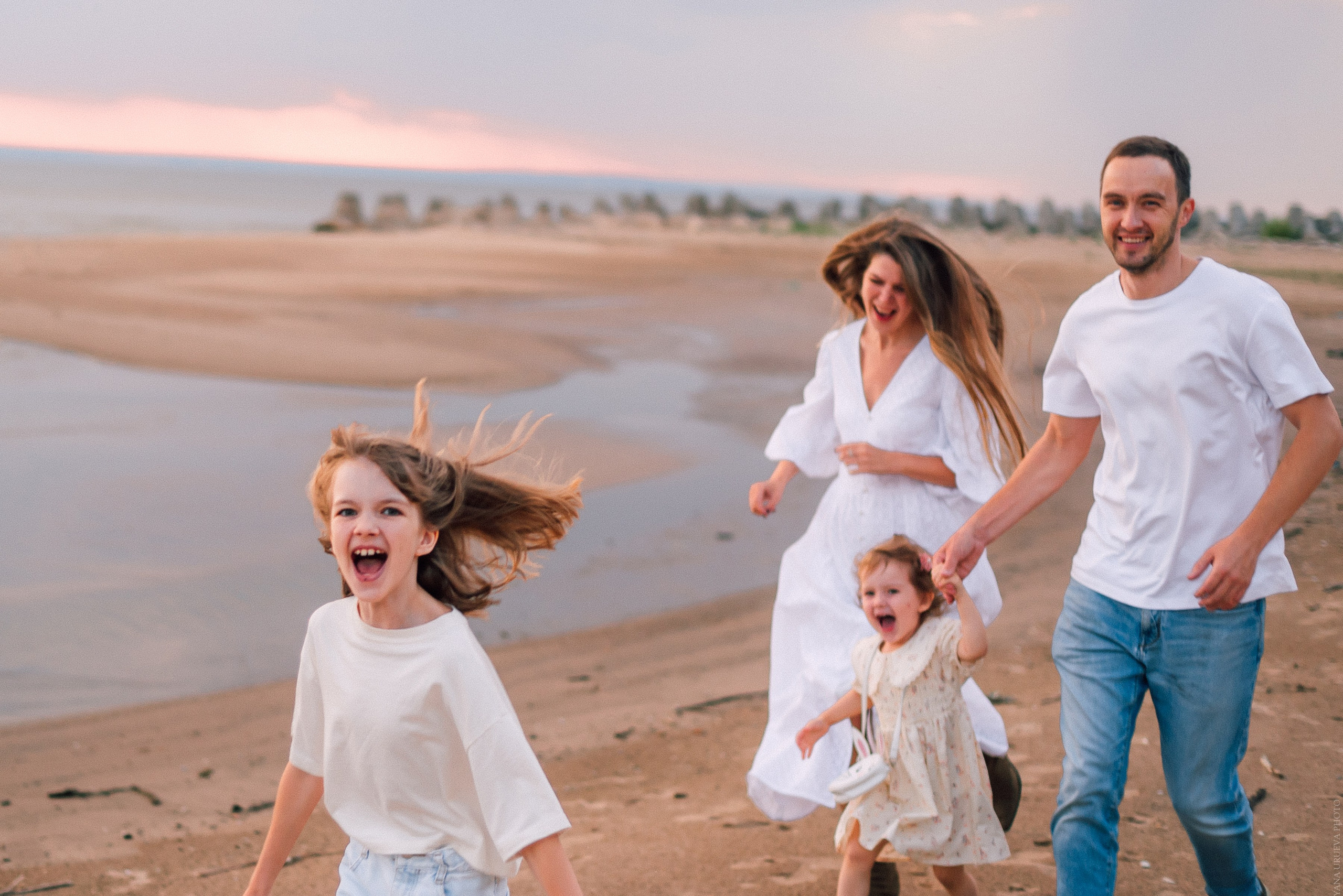 Семья с детьми бегают по берегу реки