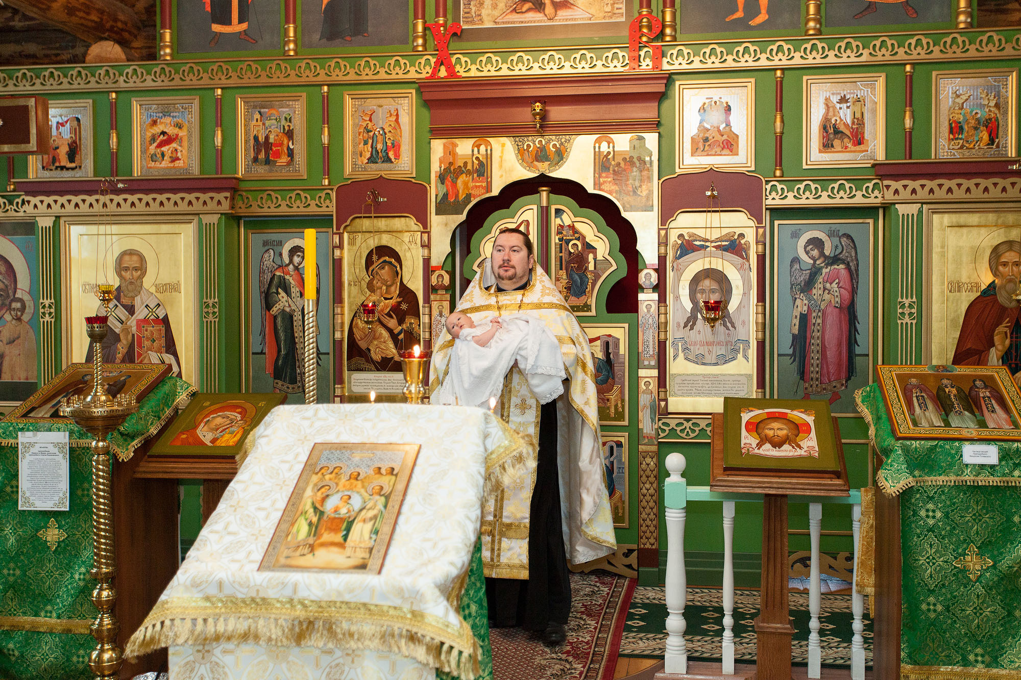 Священник выходит из алтаря с младенцем на руках.