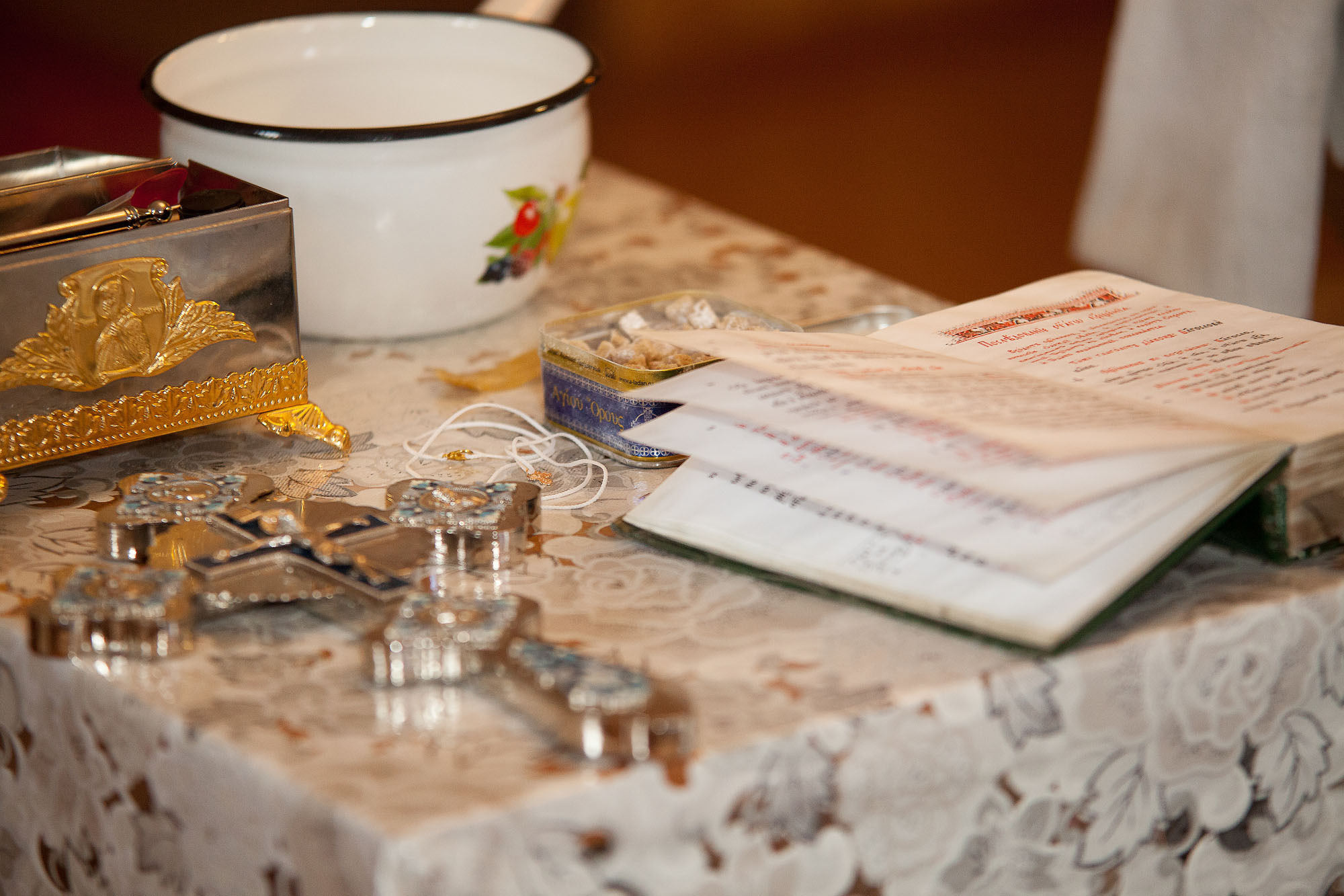 Вещи для крещения на столе: крест серебряный, книга церковная, белый ковшик.