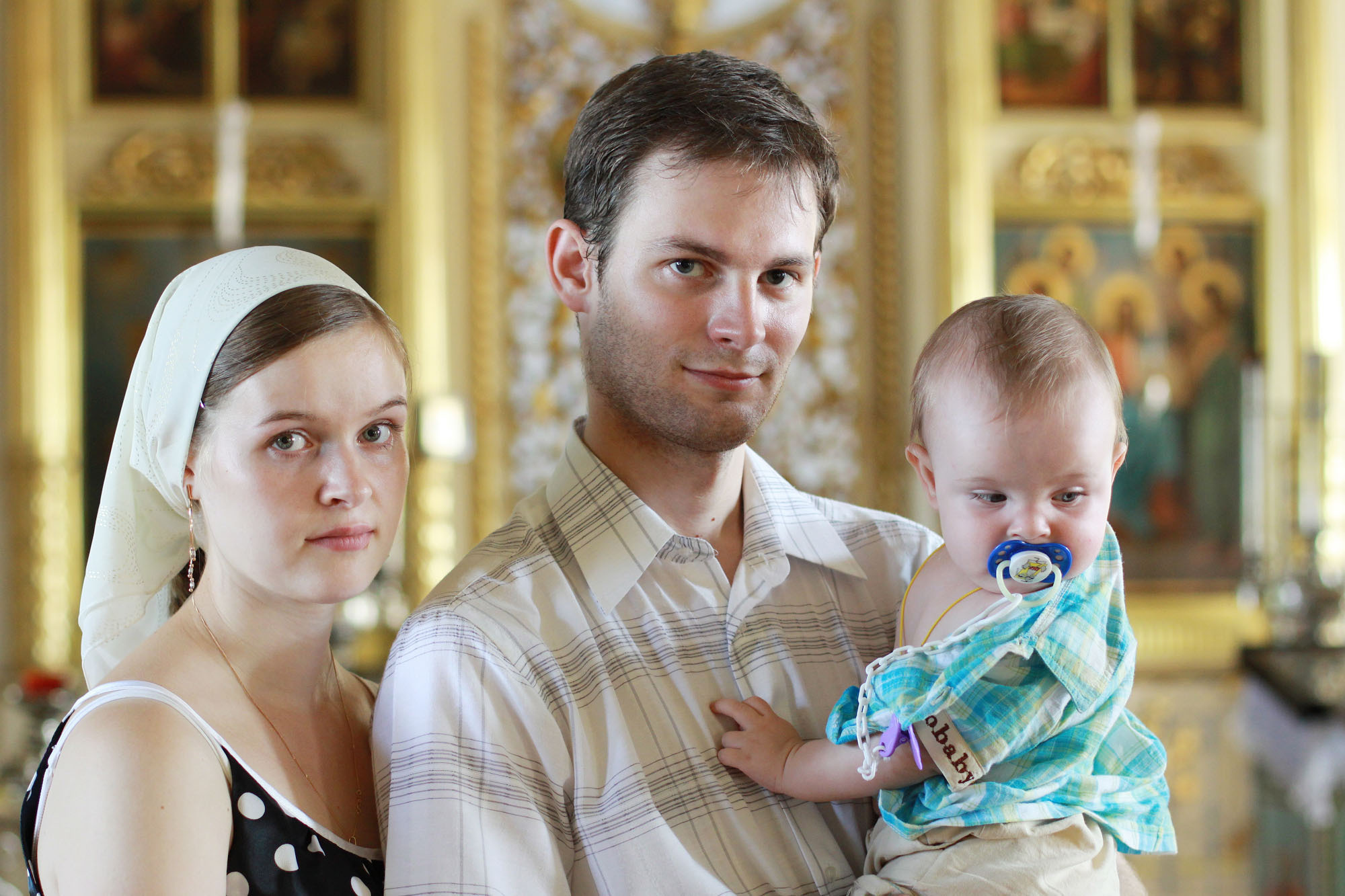 Женщина и мужчина с ребенком на руках стоят в церкви на фоне алтаря.