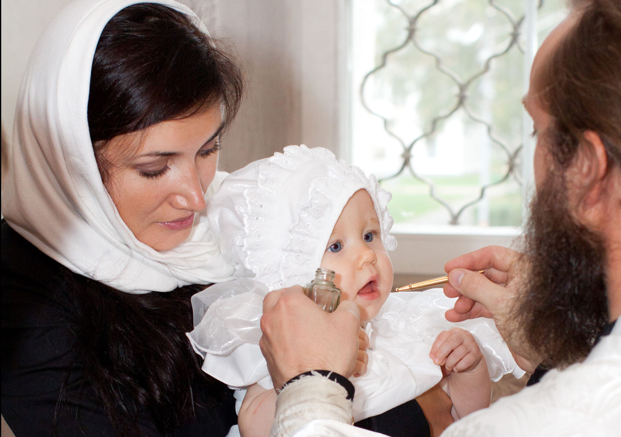 Священник с бородой делает помазание девочке в платке.