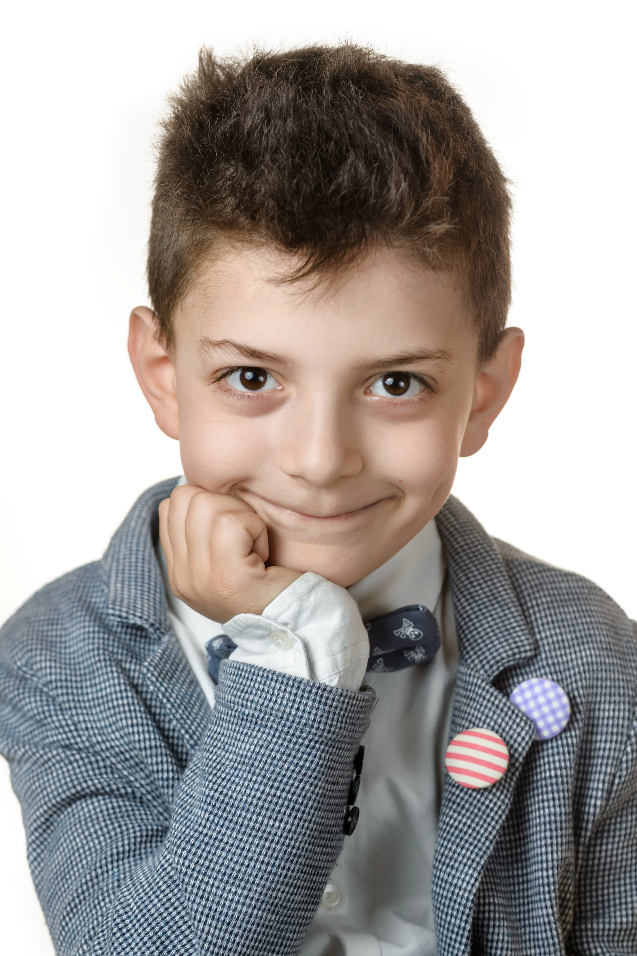 Мальчик в сером пиджаке с рукой у подбородка на светлом фоне