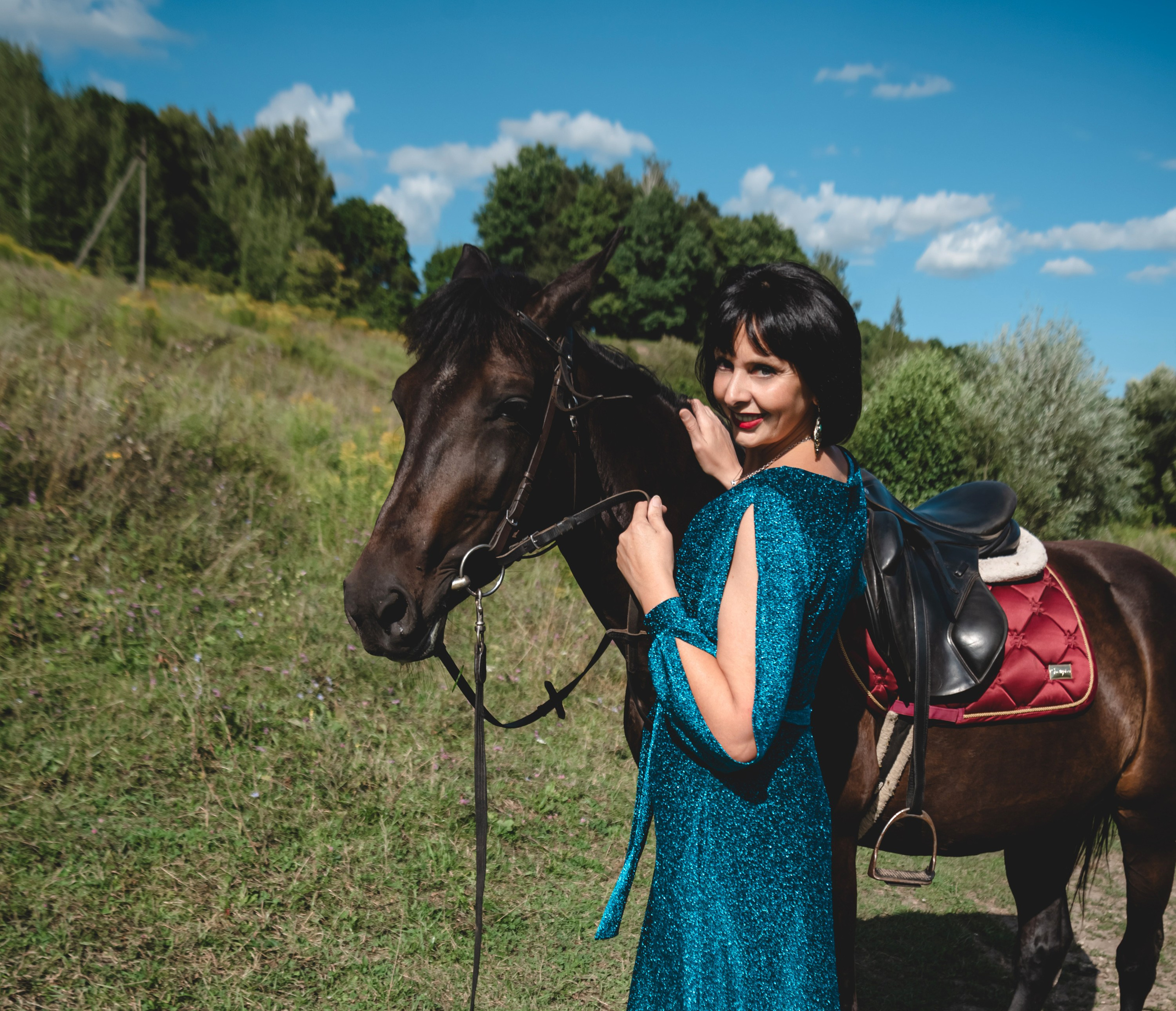 На фото женщина в зеленом платье стоит с лошадью.