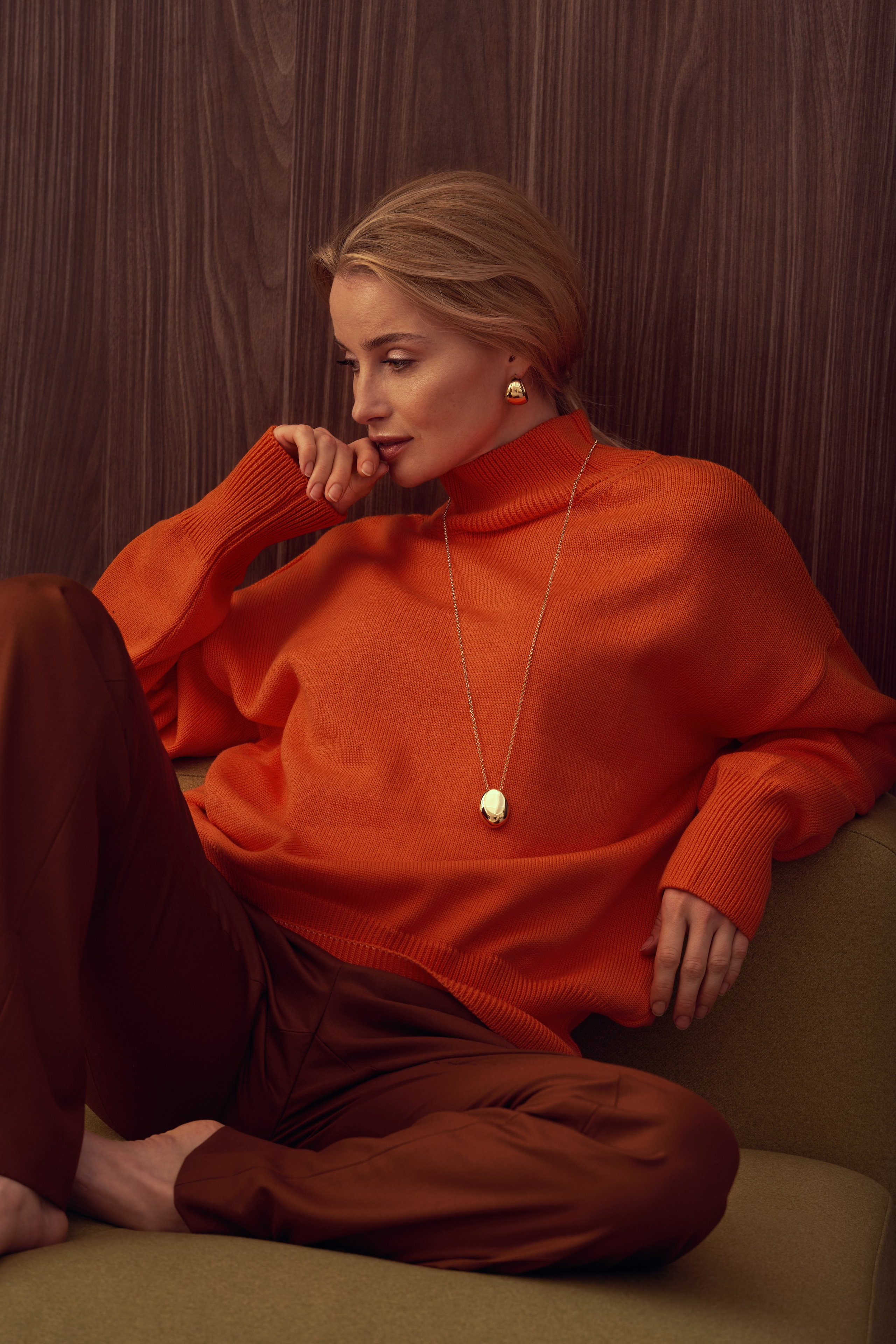 Съемка лукбука, мягкий свет, девушка в оранжевом свитере и коричневых брюках сидит на зеленом пуфе