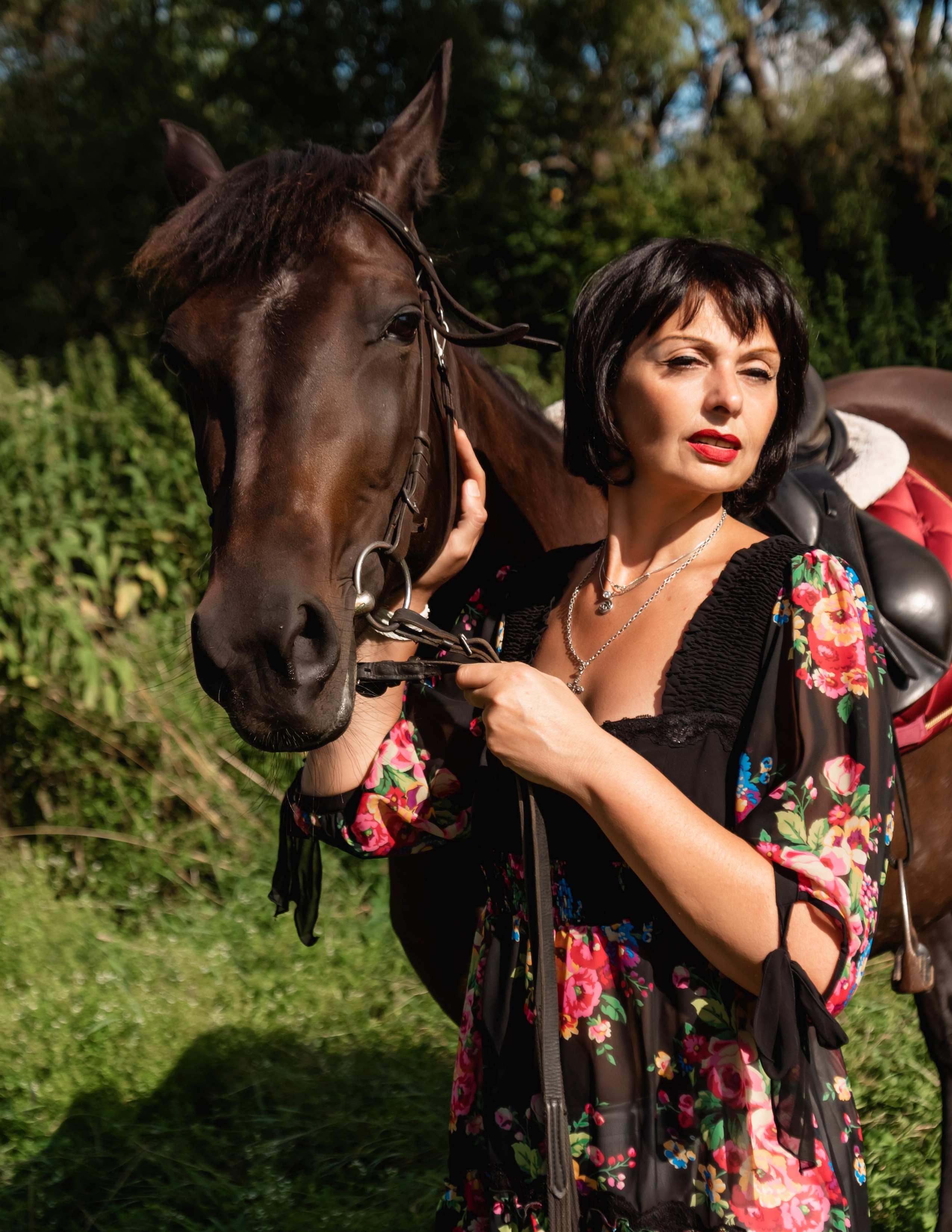 На фото женщина в бежевом платье с цветами стоит с лошадью.