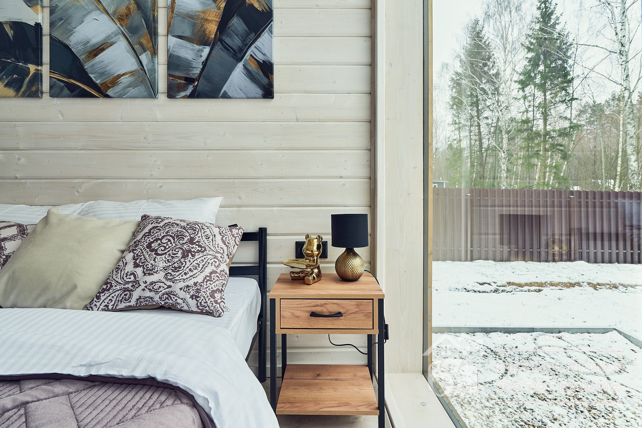 Интерьерная фотография большой спальни с ракурсом на подушки, прикроватный столик и панорамное окно загородного подмосковного дома