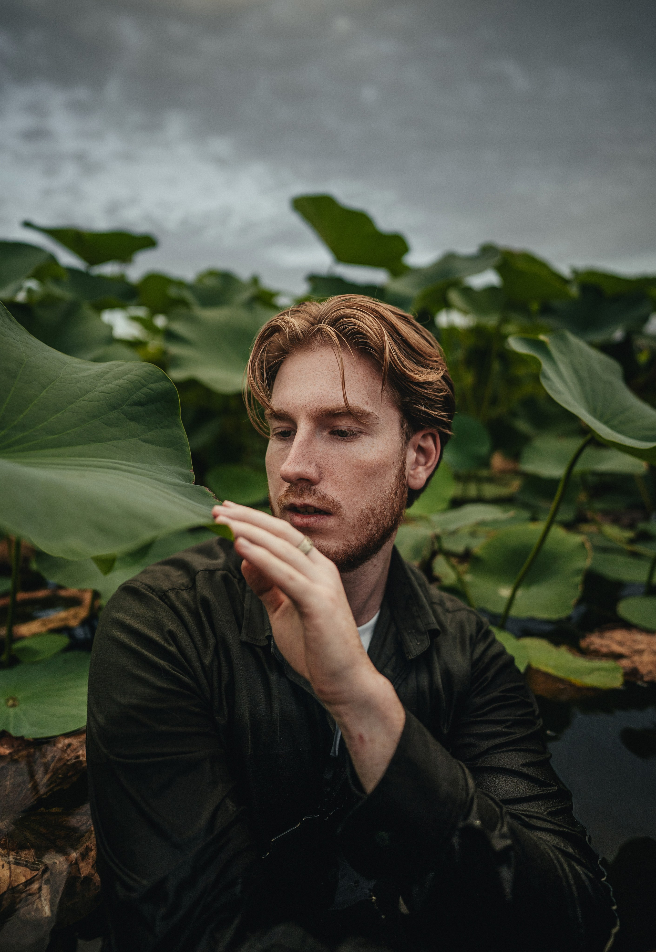 Мужчина среди огромных листьев лотоса. Смотрит вдаль, держа лист рукой