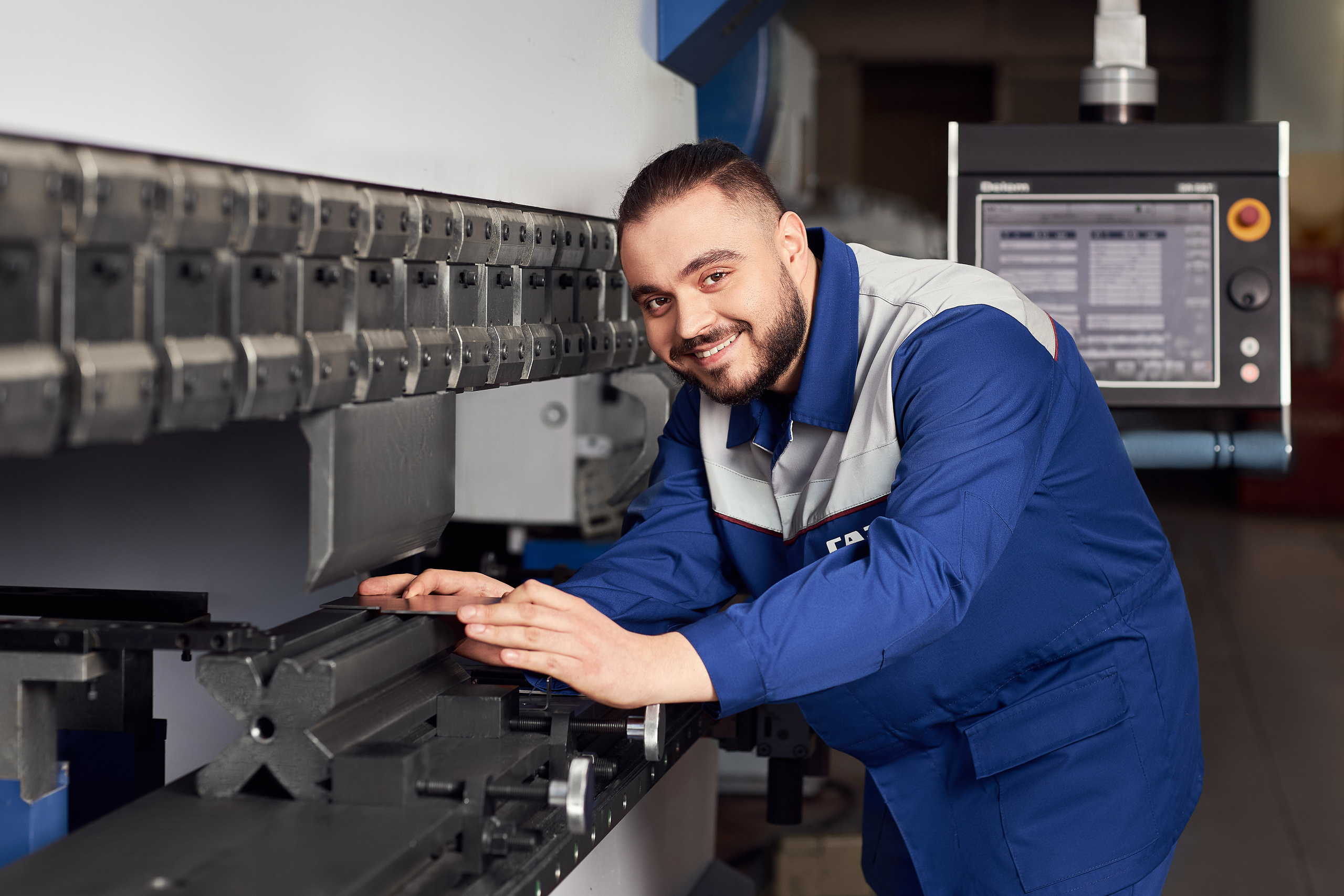 Рабочий улыбается, стоя у станка. Съёмка сотрудников компании.