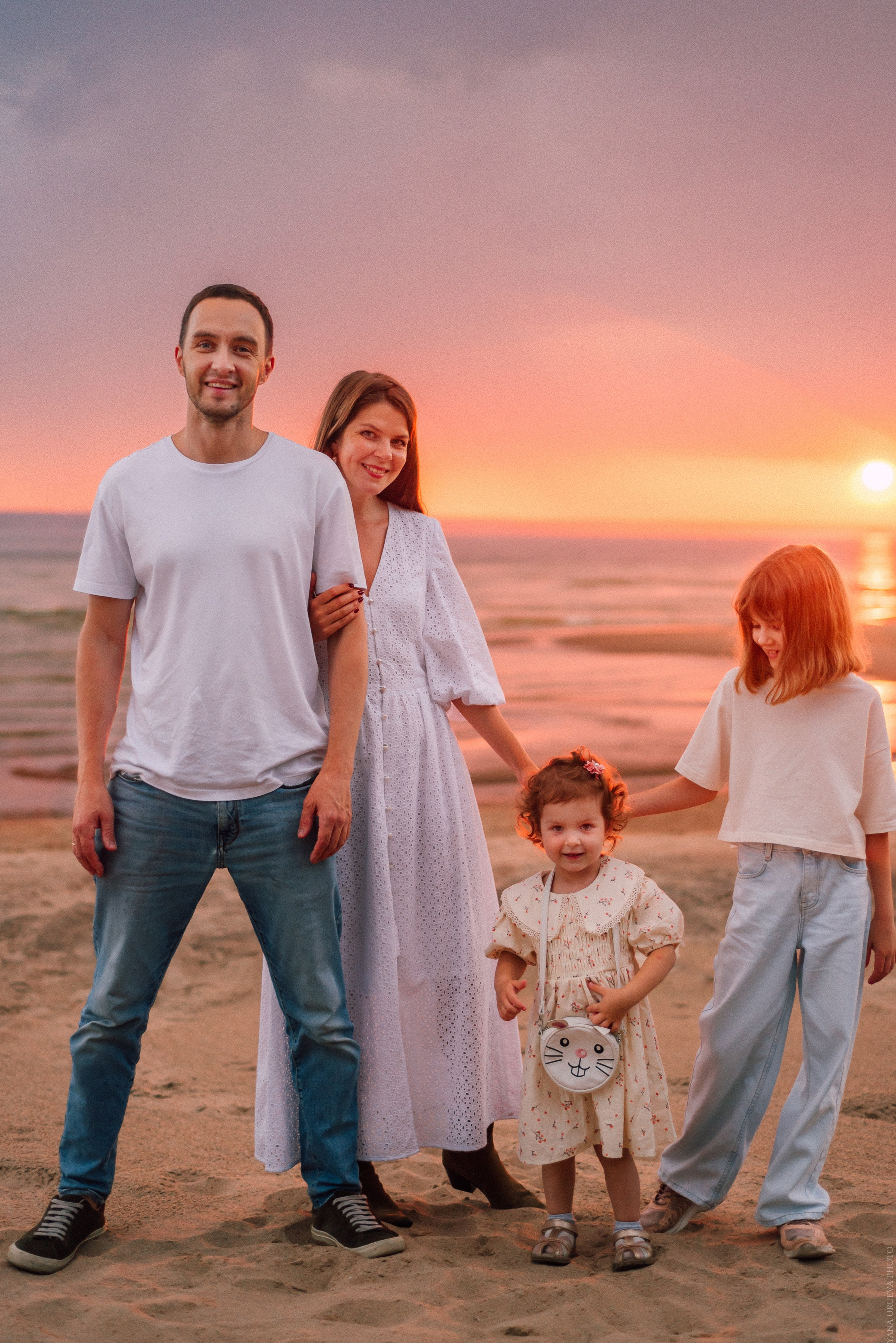 Семья с детьми в белой одежде на берегу на закате