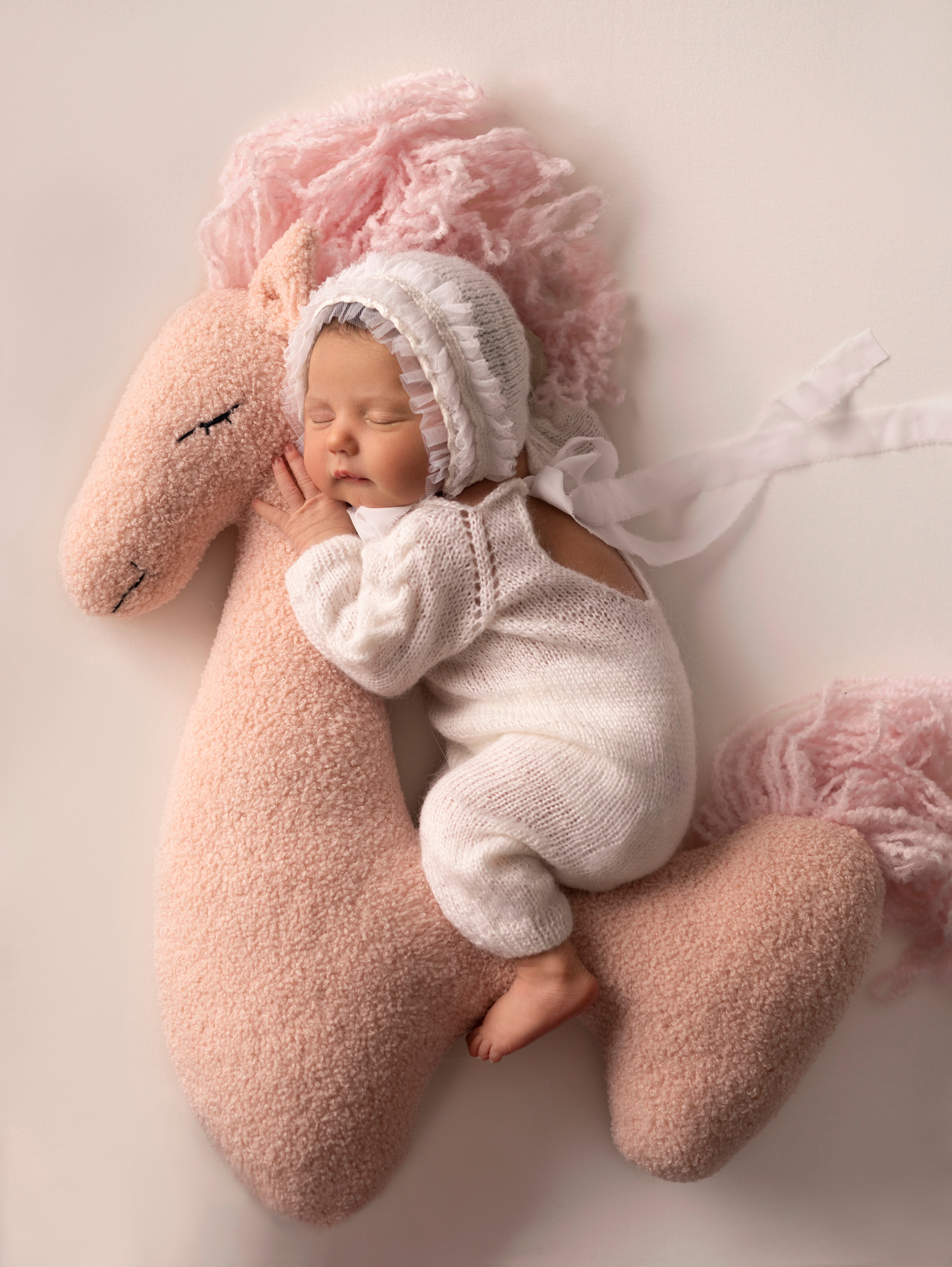 новорожденный сладко спит на белом фоне newborn фото фотосессия на лошадке пони единороге реквизит