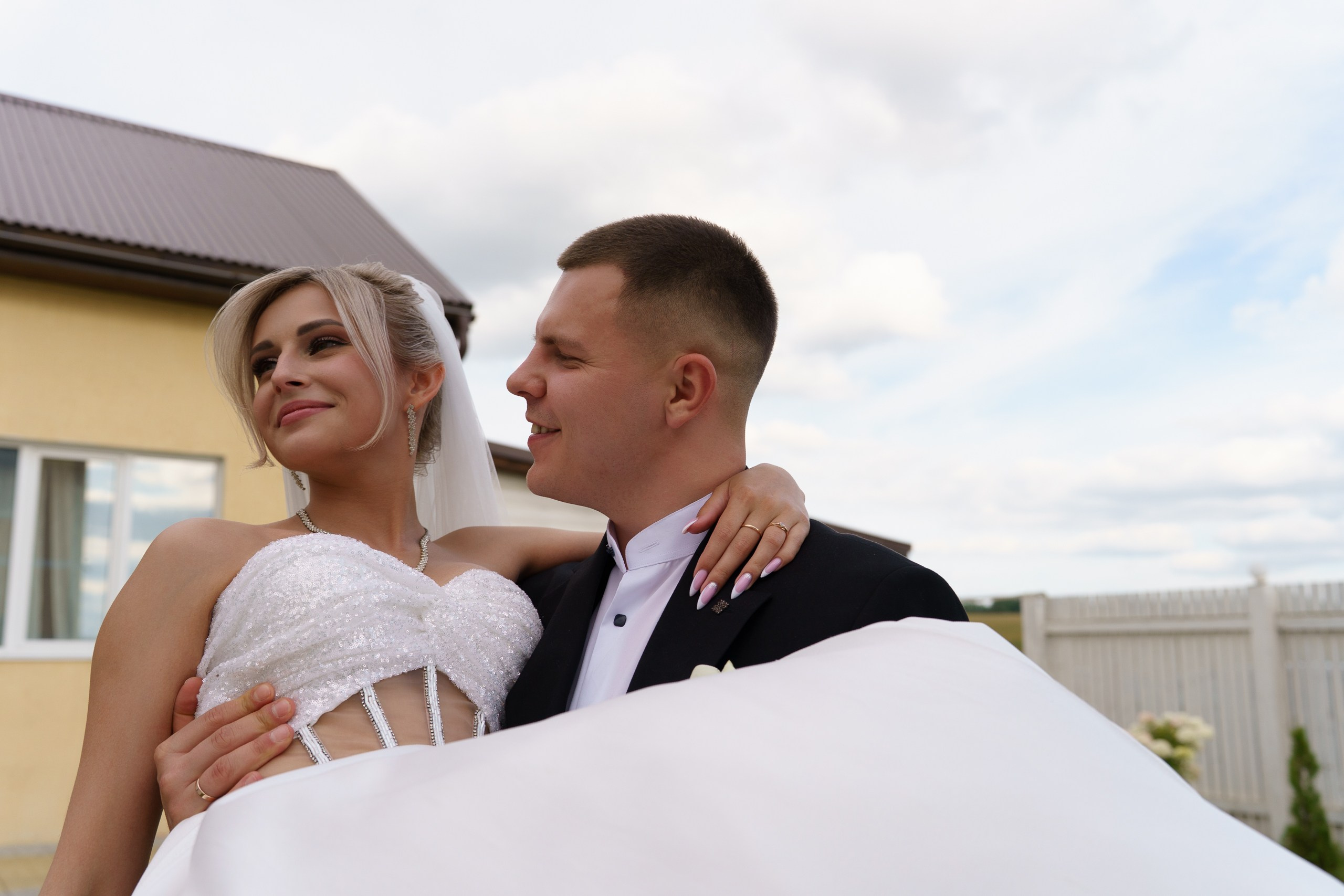 Очарование свадебного дня: пара в свадебных нарядах на фоне загородного дома. Невеста в блестящем белом платье выглядит как принцесса, а жених в классическом чёрном костюме — воплощение стиля и надёжности | финальные свадебные фото Екатеринбург