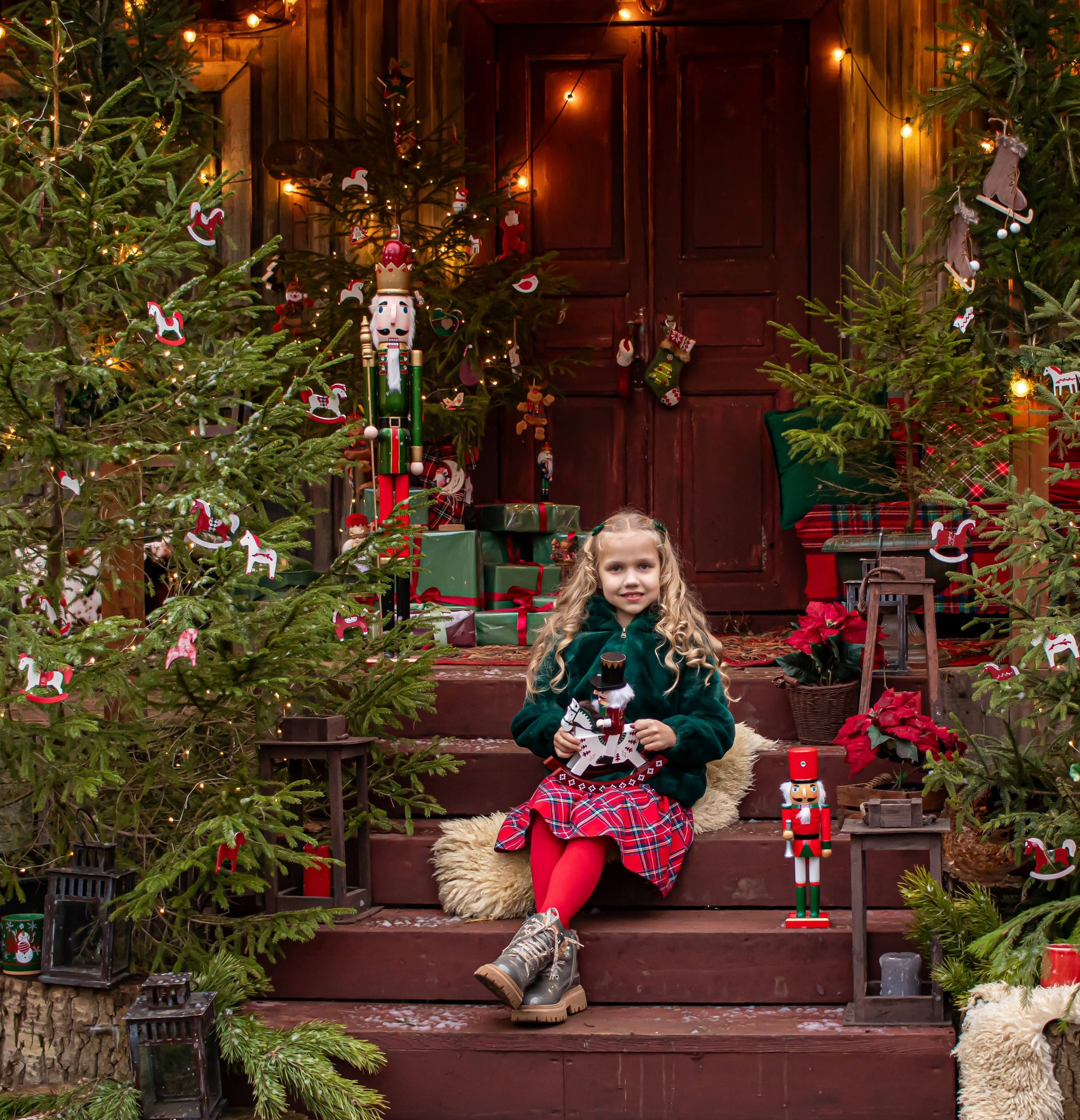 Девочка улыбается, сидя среди еловых веток и подарков, новогодняя фотосессия, фотограф Карасёва Елена"