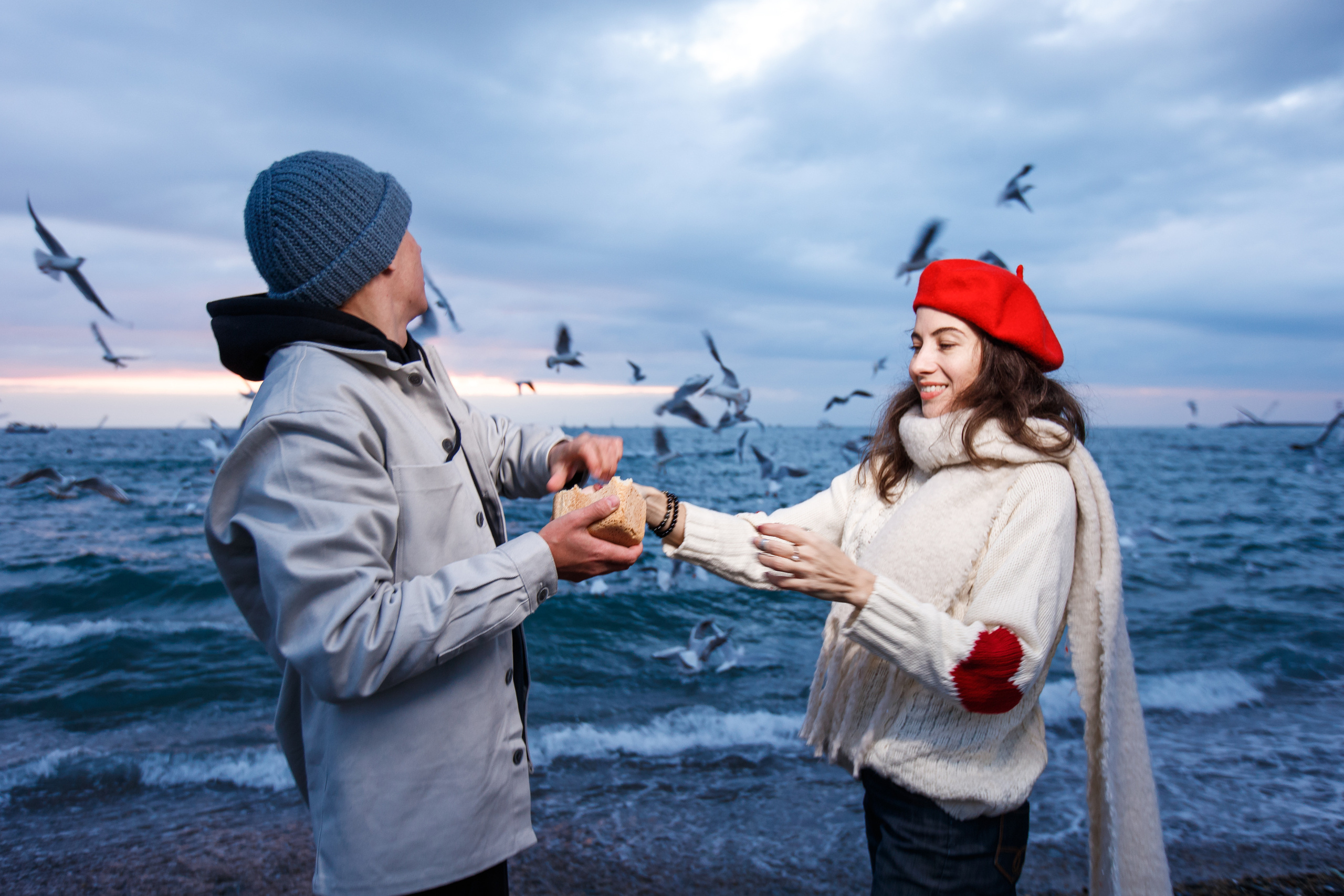 Парень и девушка в красном берите кормят чайник на фоне зимнего штормового моря
