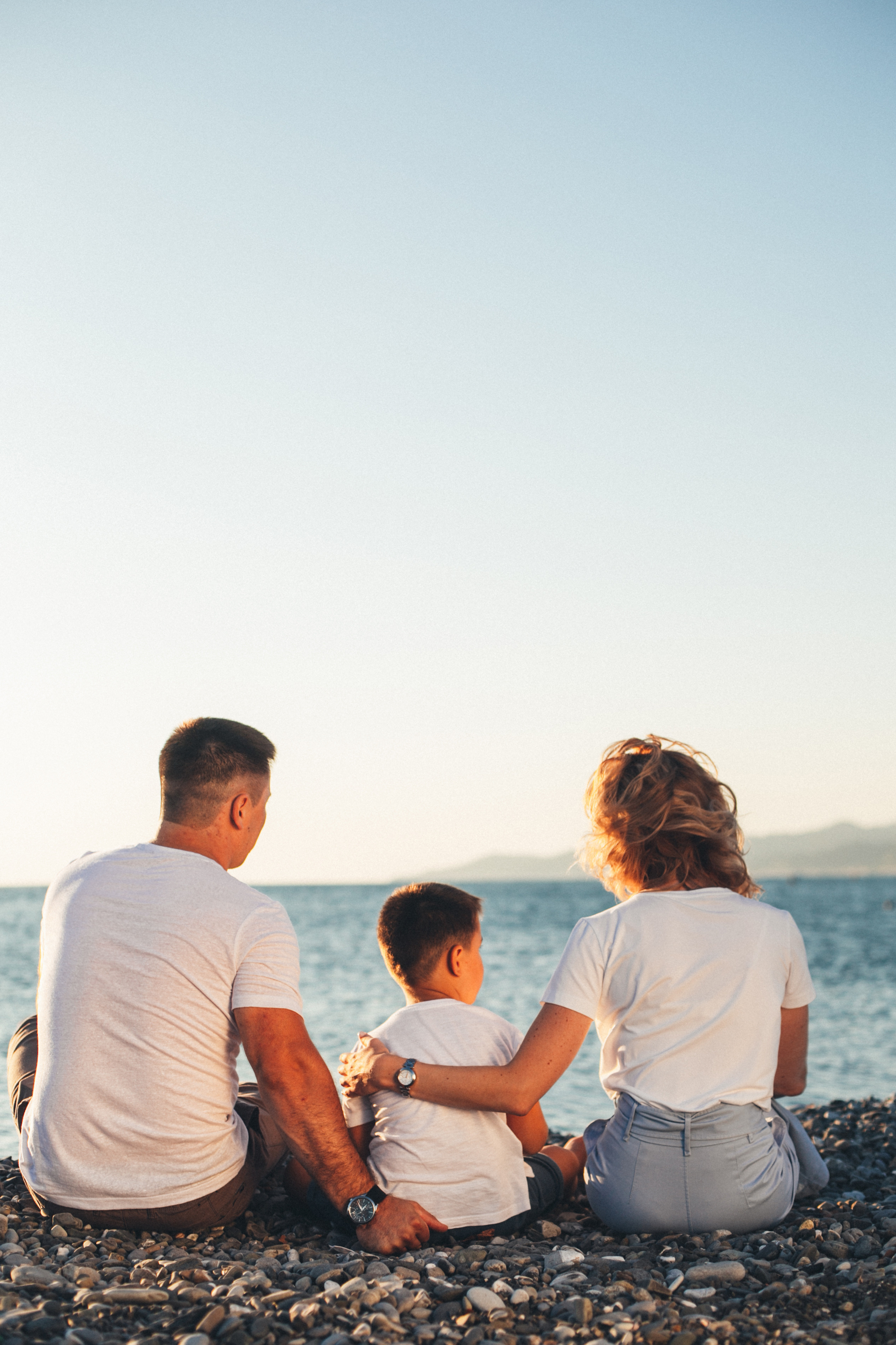 Семья сидит спиной к камере на фоне моря и заката