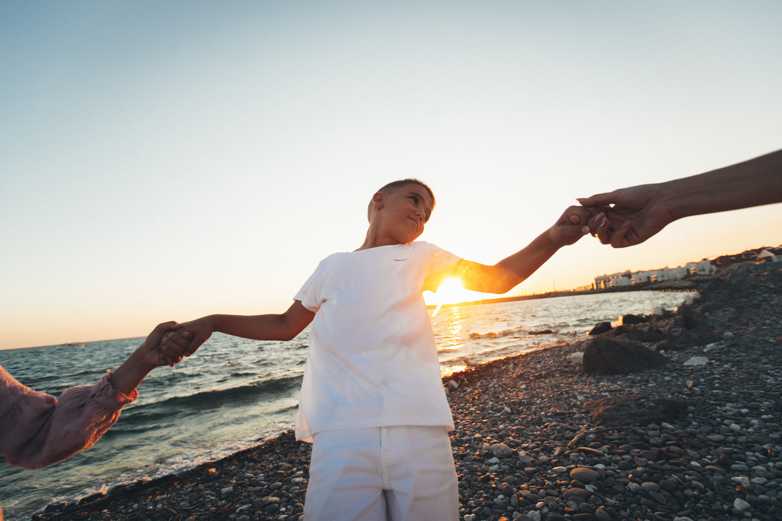 Мальчик, которого держит с двух сторон за руки на фоне моря и заката