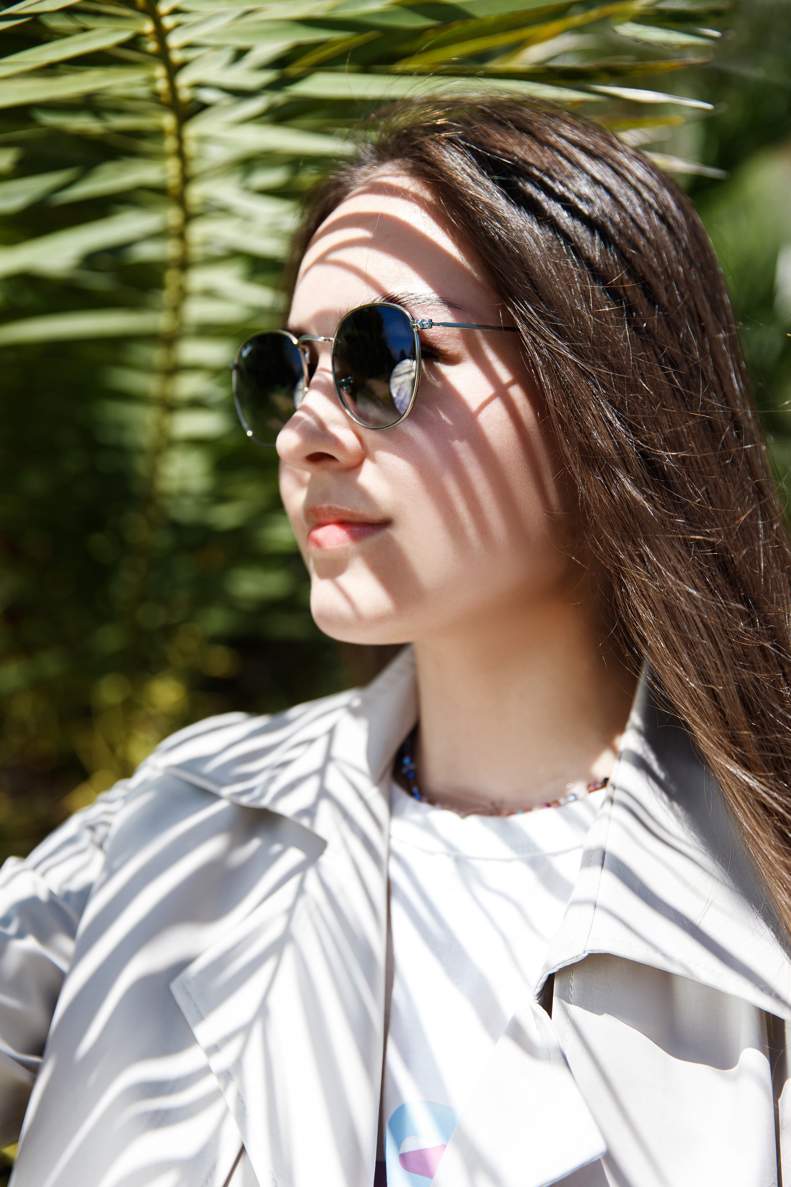 Девочка в очках RayBan на фоне пальмы в бежевом тренче
