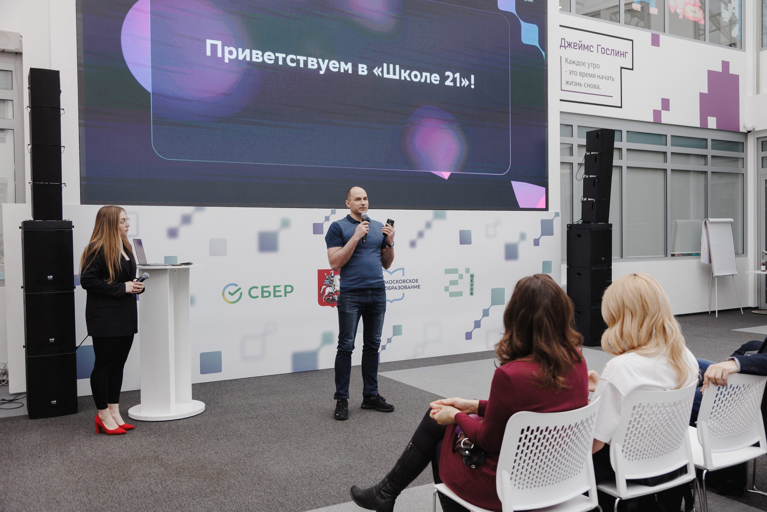 Репортаж с мероприятия: спикер у микрофона, внимательная аудитория на заднем плане.