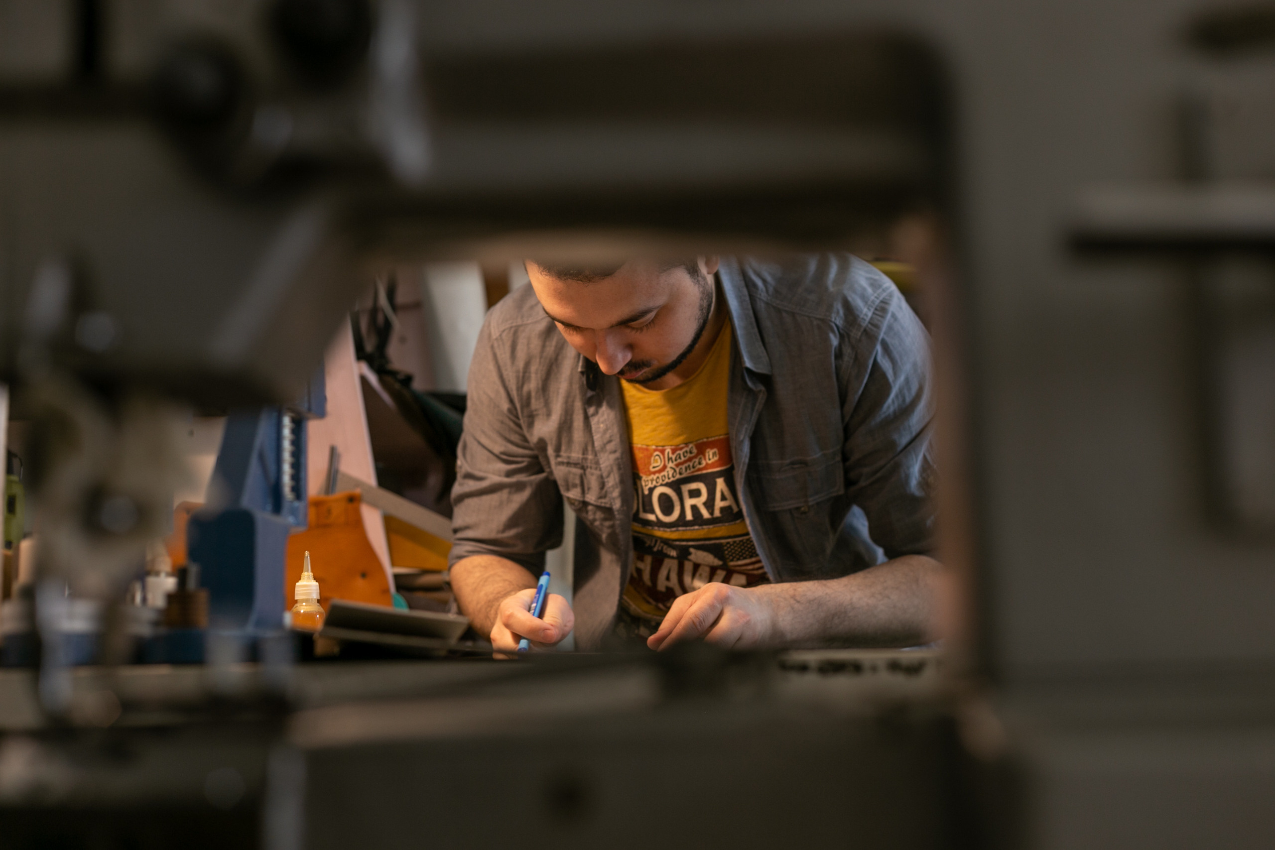 Вид сквозь швейную машинку на мастера кожевника, который шьет из натуральной кожи. Бородатый мужчина мастер ремесленник в мастерской.