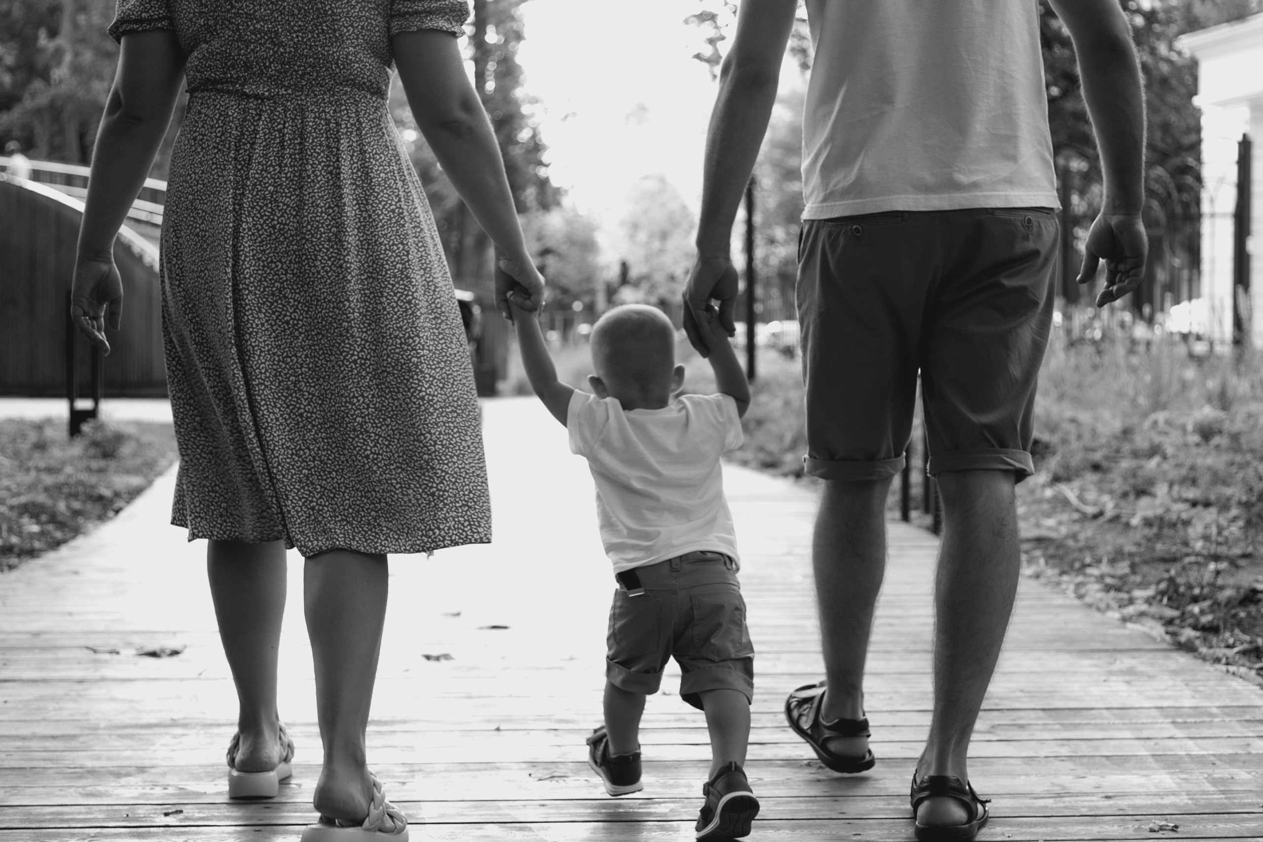 Фото со спины на родителей и маленького ребенка, которые держатся за руки. Черно-белое фото семьи.