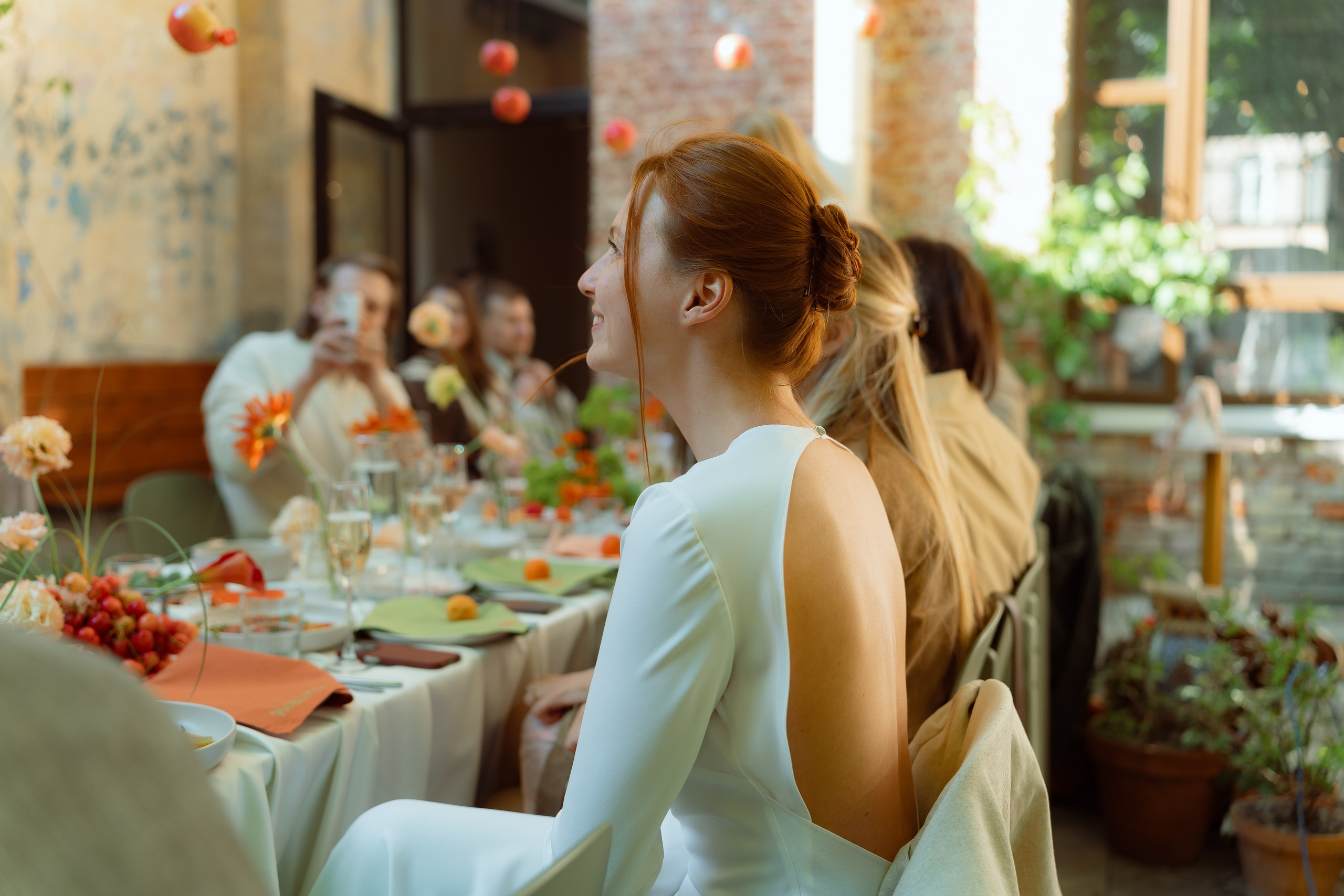 Мария сидит за длинным столом, открытая спина платья на фоне декора