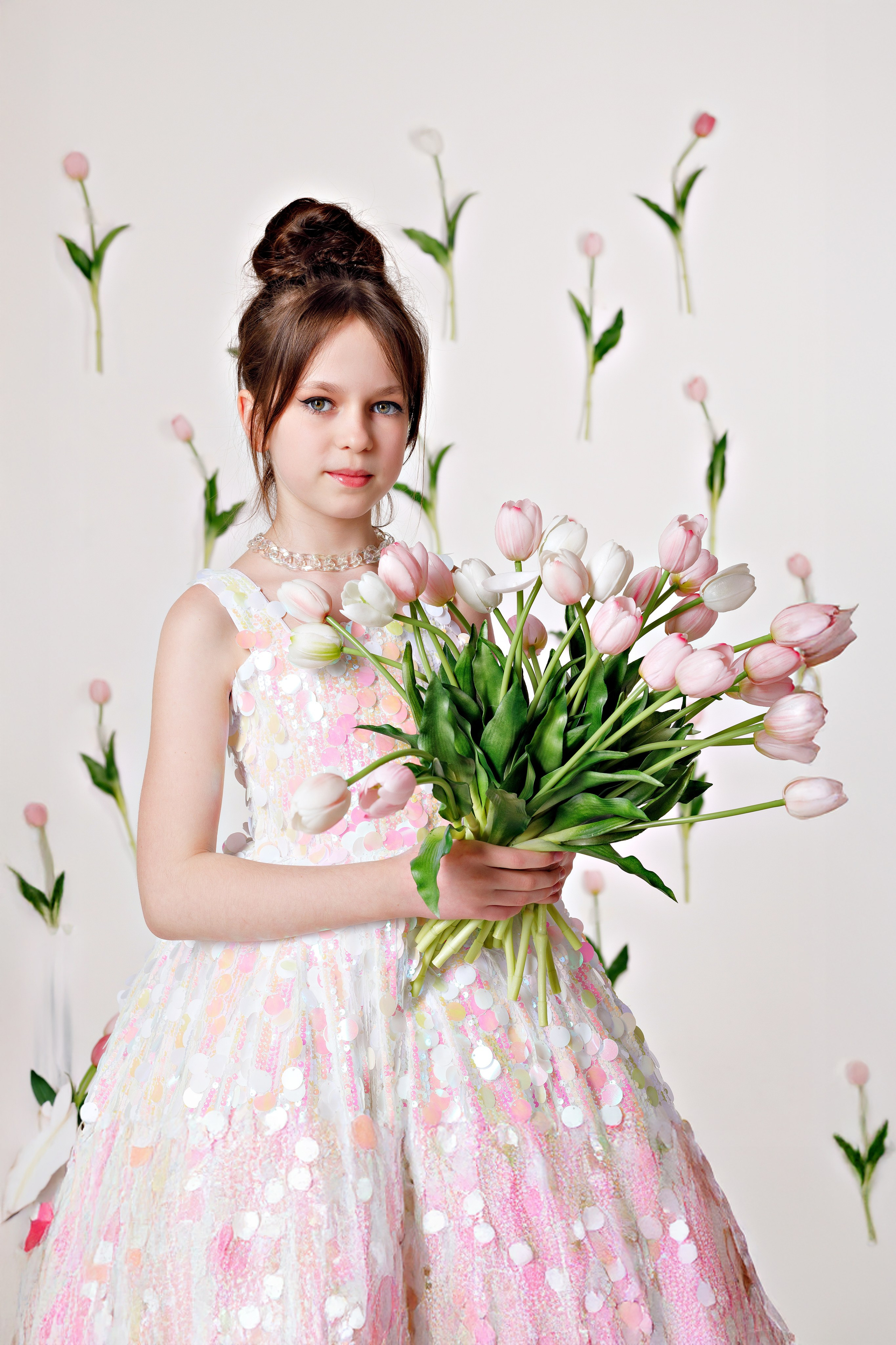Девочка в блестящем платье с букетом тюльпанов на фоне праздничного декора в Сочи
