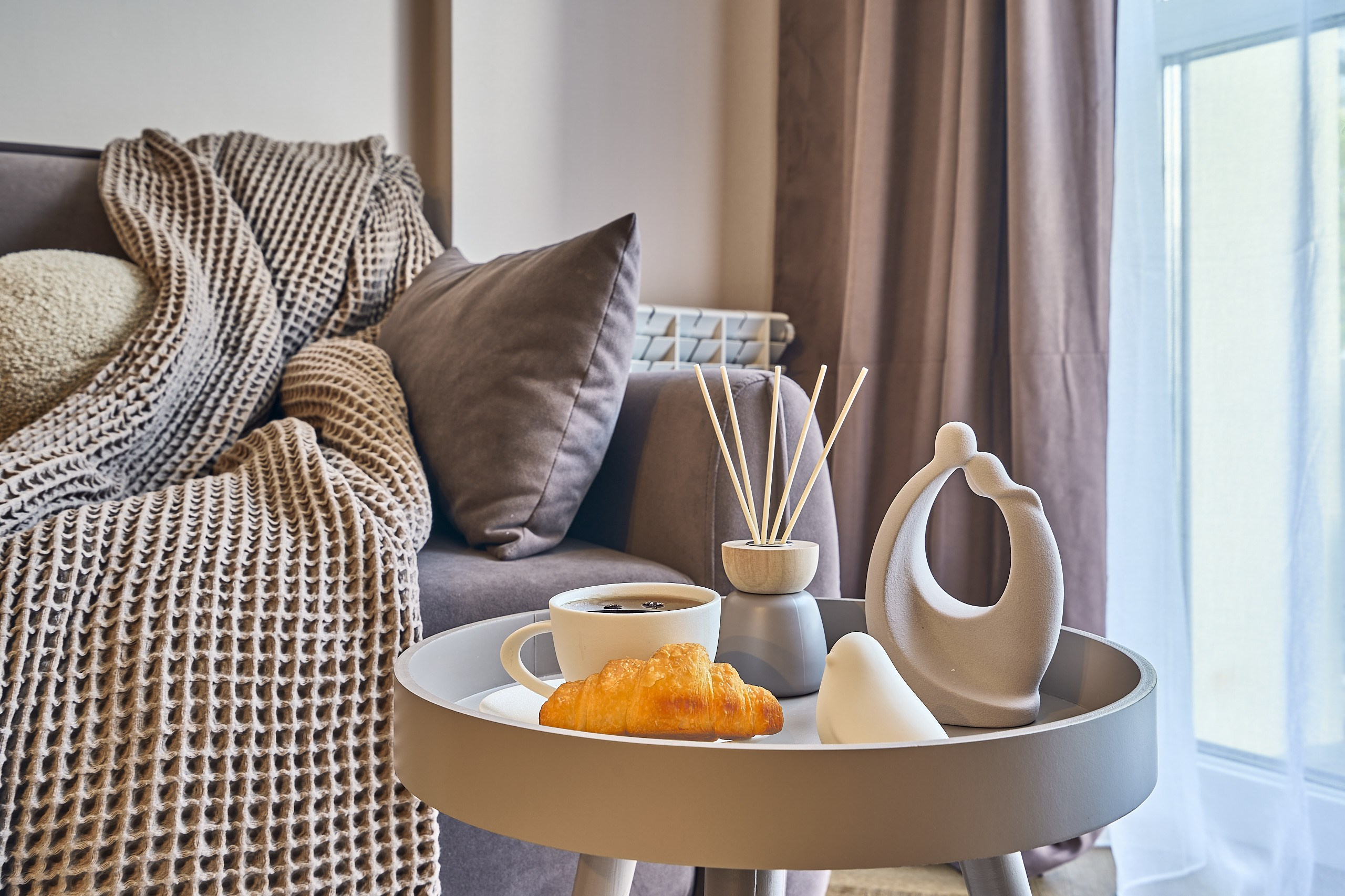 Интерьерная съемка: апартаменты в посуточную аренду, композиция на придиванном столике: кофе, свежий и аппетитный круассан, арома палочки, интерьерные фигурки